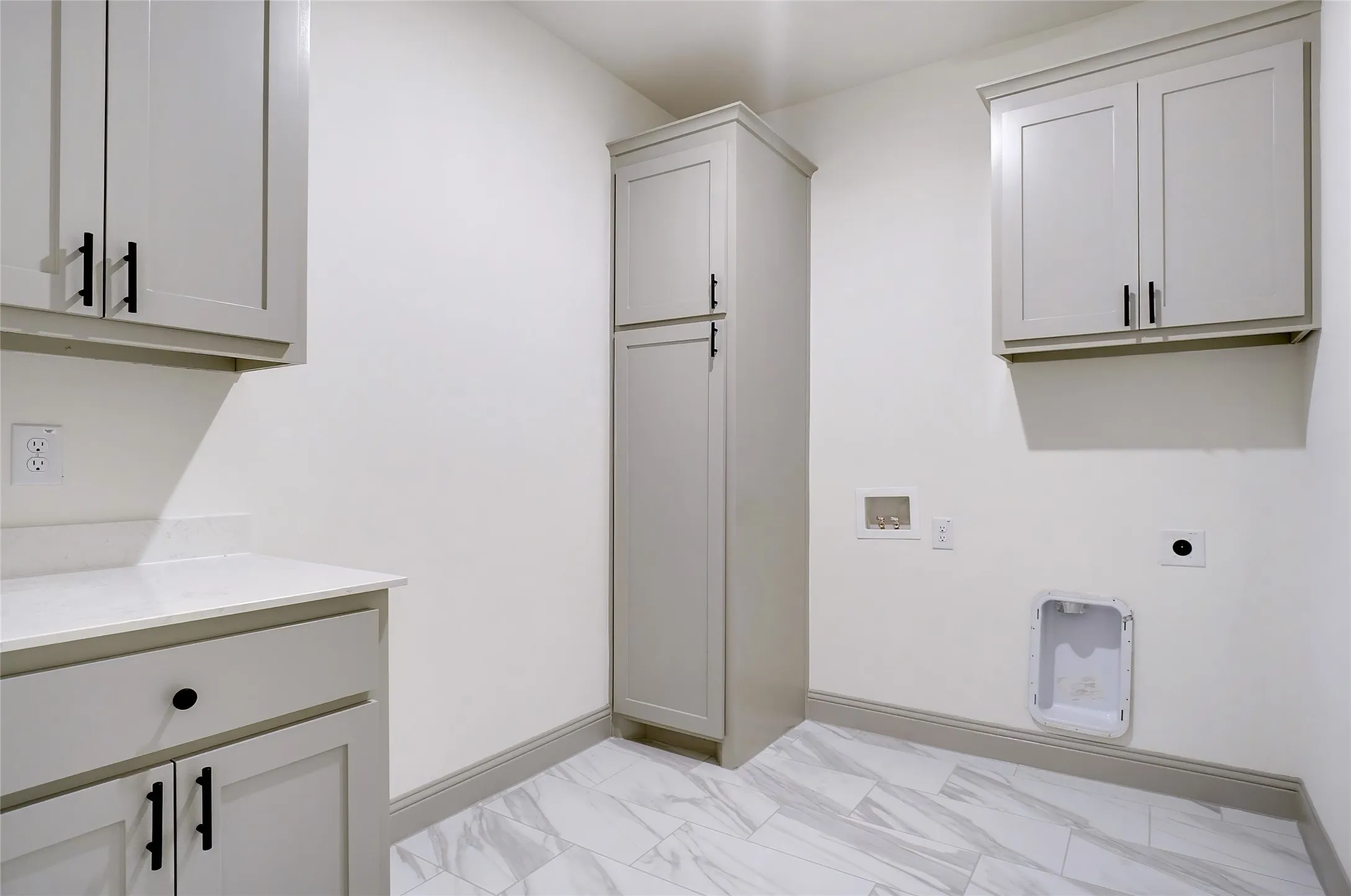 Utility room featuring light grey cabinetry with black hardware, white countertop, and patterned tile flooring