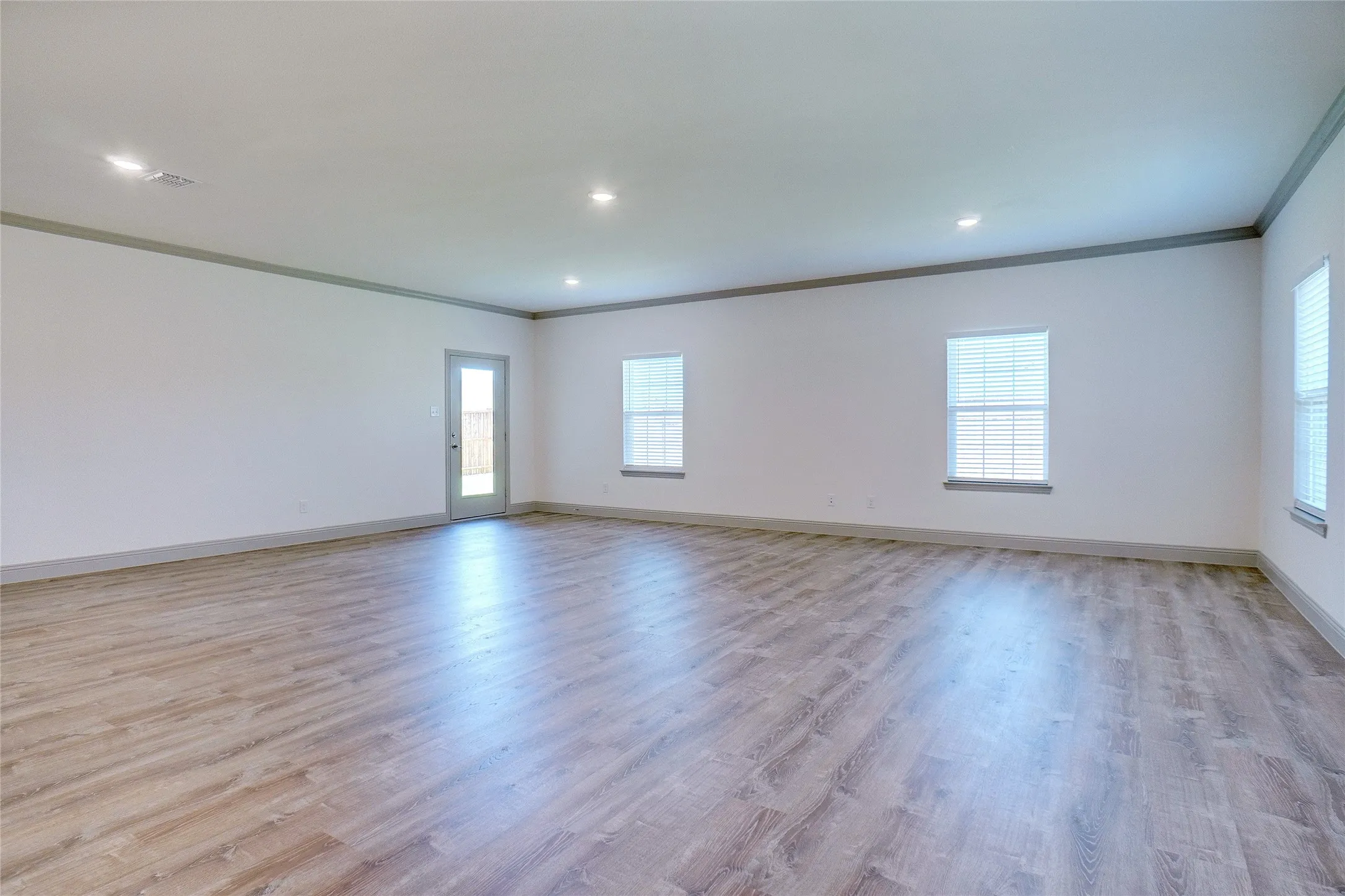 Spacious room featuring wood-finish flooring, recessed lighting, and multiple windows with blinds