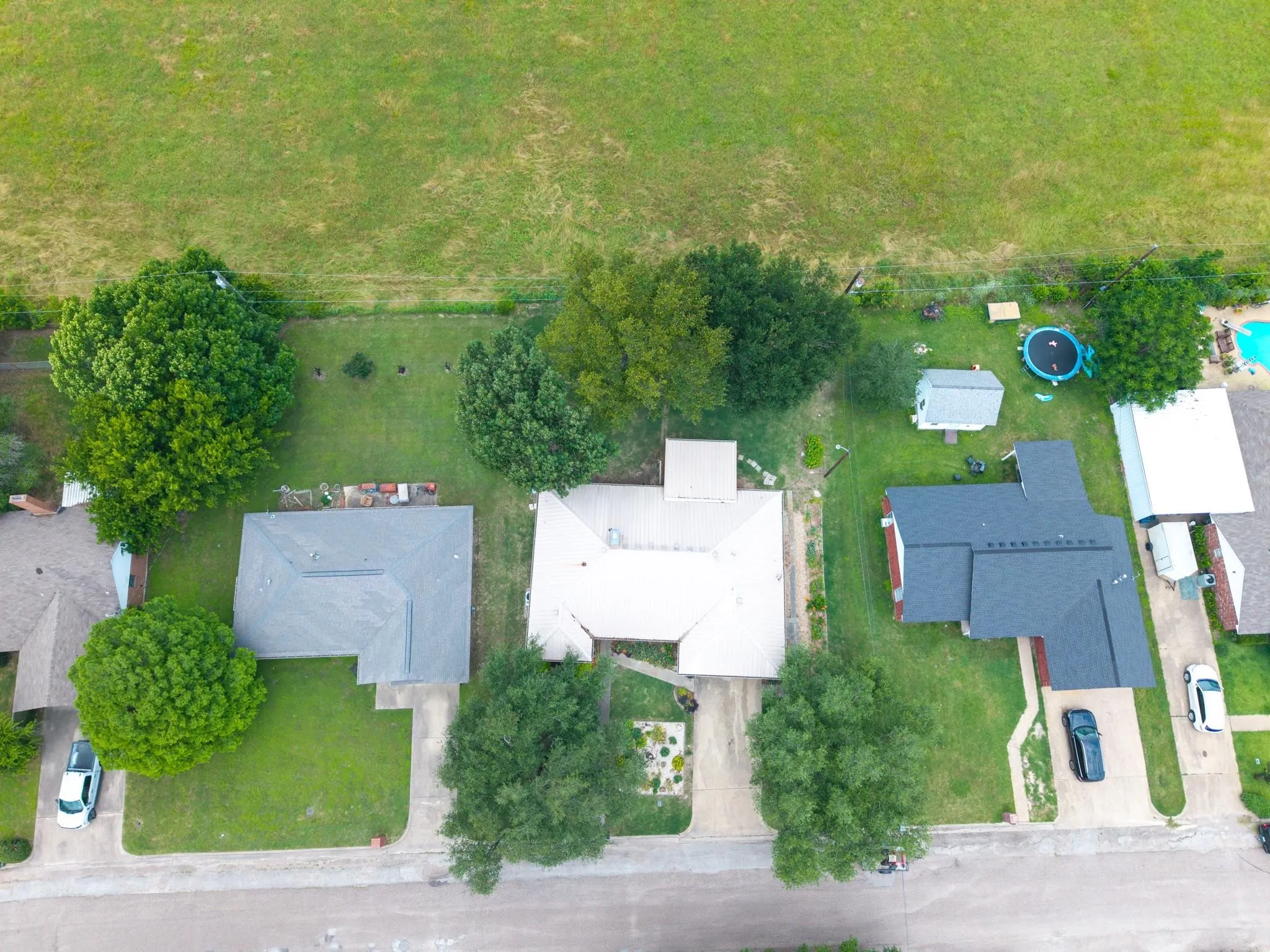 Aerial perspective showcasing three residential properties with varied rooflines and surrounding green spaces