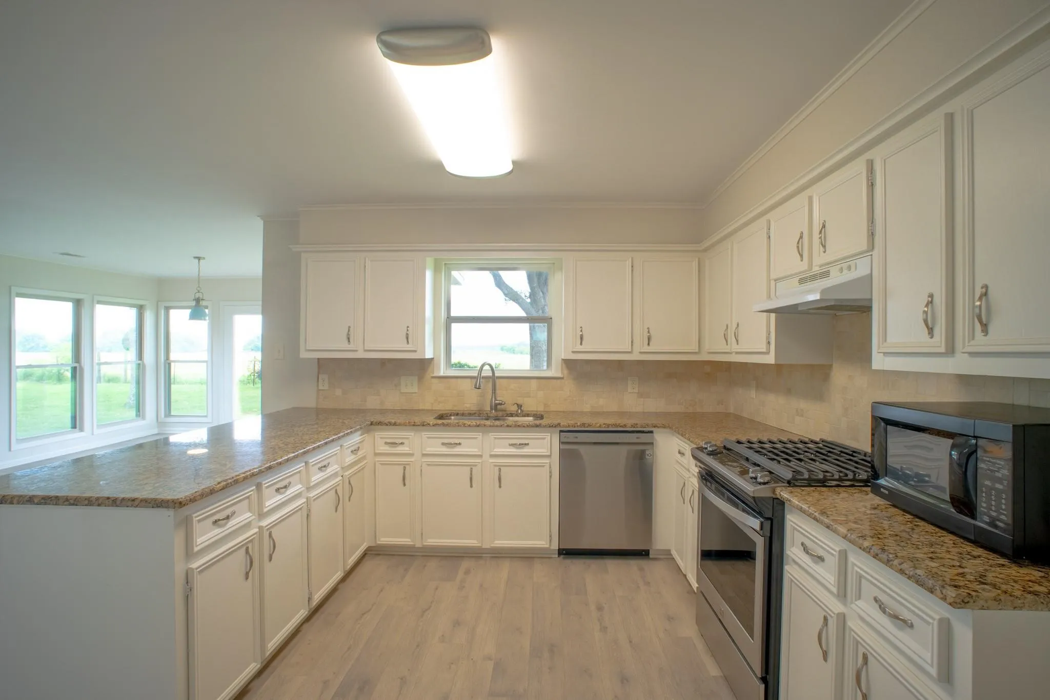 U-shaped kitchen featuring wood-finish flooring, light-toned cabinetry, granite countertops, and a tile backsplash