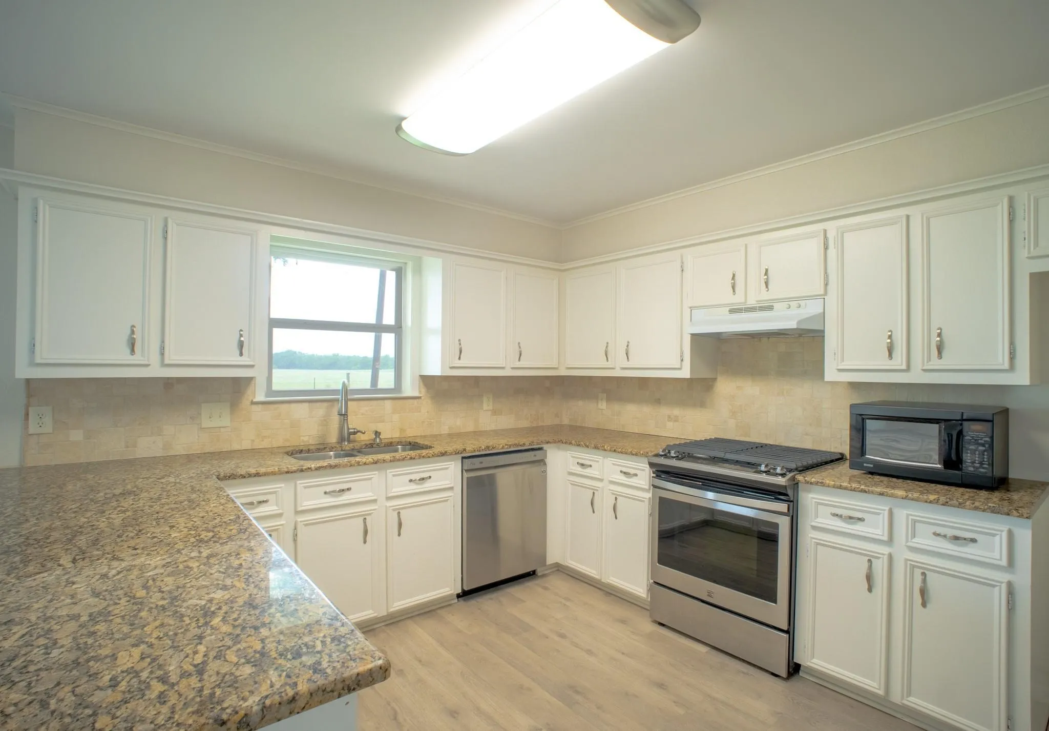 Kitchen featuring extensive stone-finish countertops, white cabinetry, a stainless steel dishwasher, and wood-finish flooring