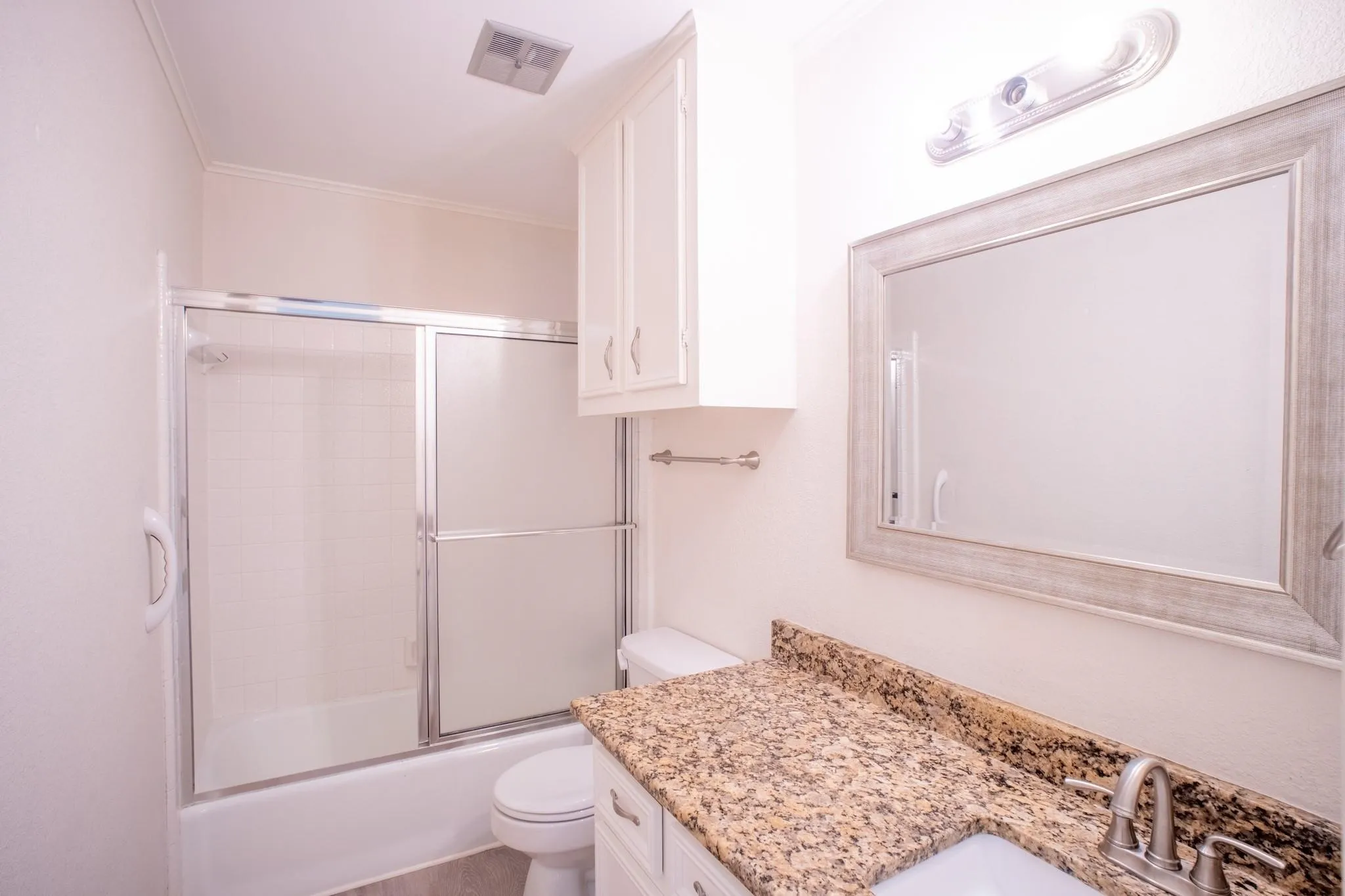 Bathroom featuring a vanity with a granite-style countertop and undermount sink, framed mirror, and a shower-tub combination with sliding glass doors