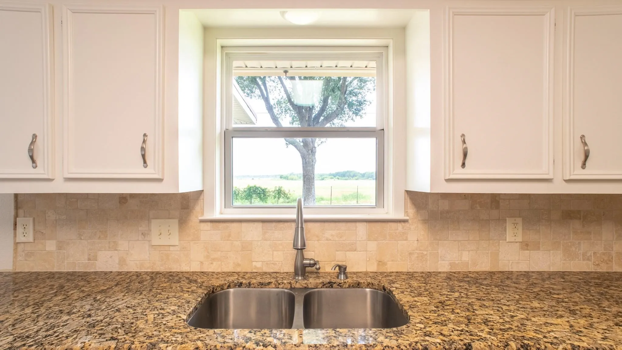 Kitchen sink area featuring a dual basin stainless steel sink, a chrome faucet, and a tile backsplash