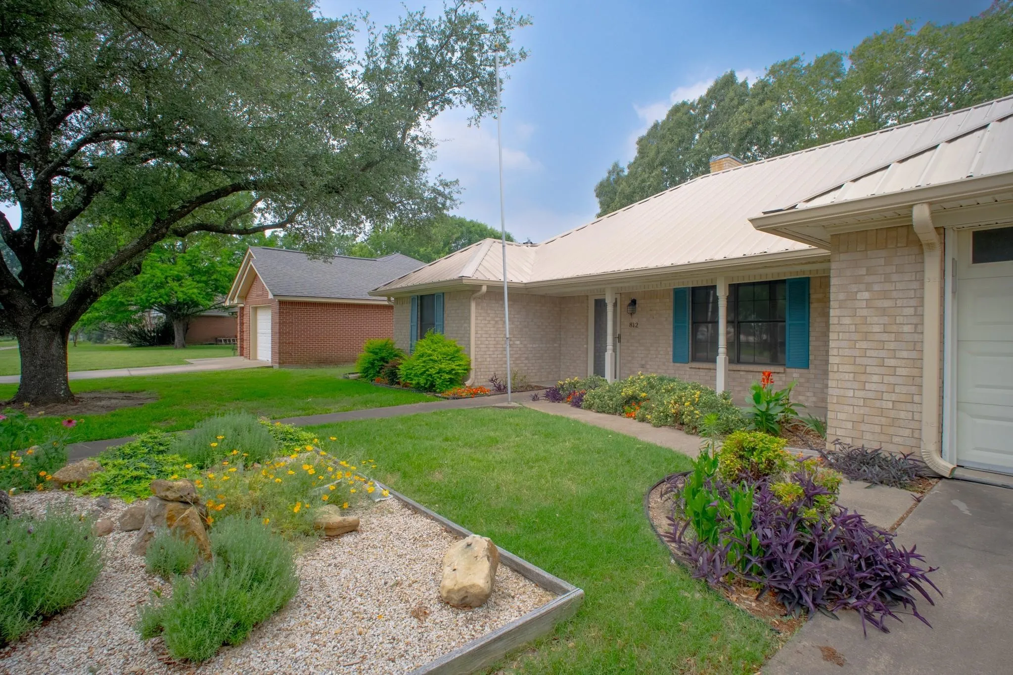 Light-colored brick exterior with teal window shutters, a white metal roof, and an attached garage