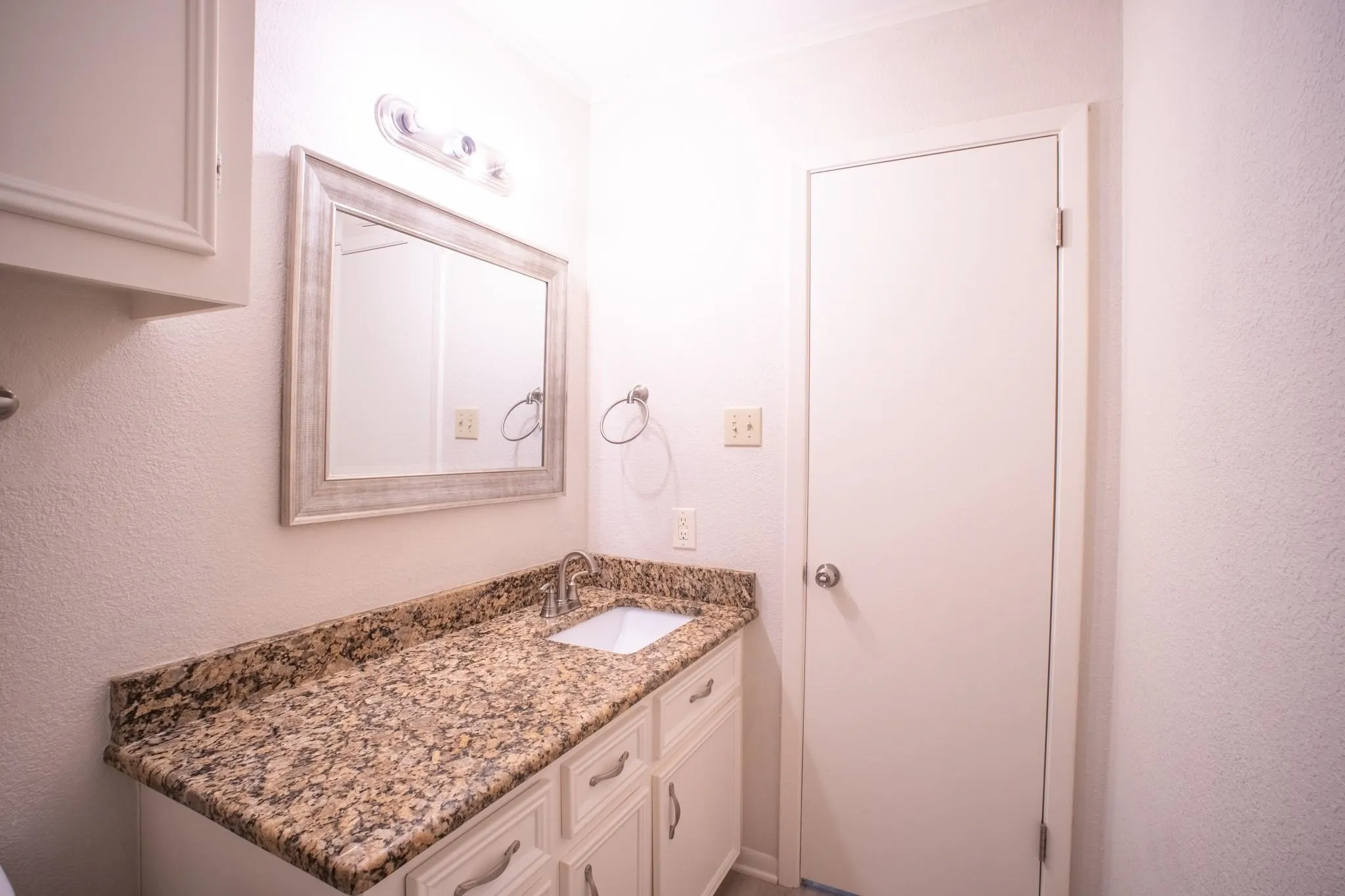Bathroom vanity with a granite-style countertop, undermount sink, and chrome faucet