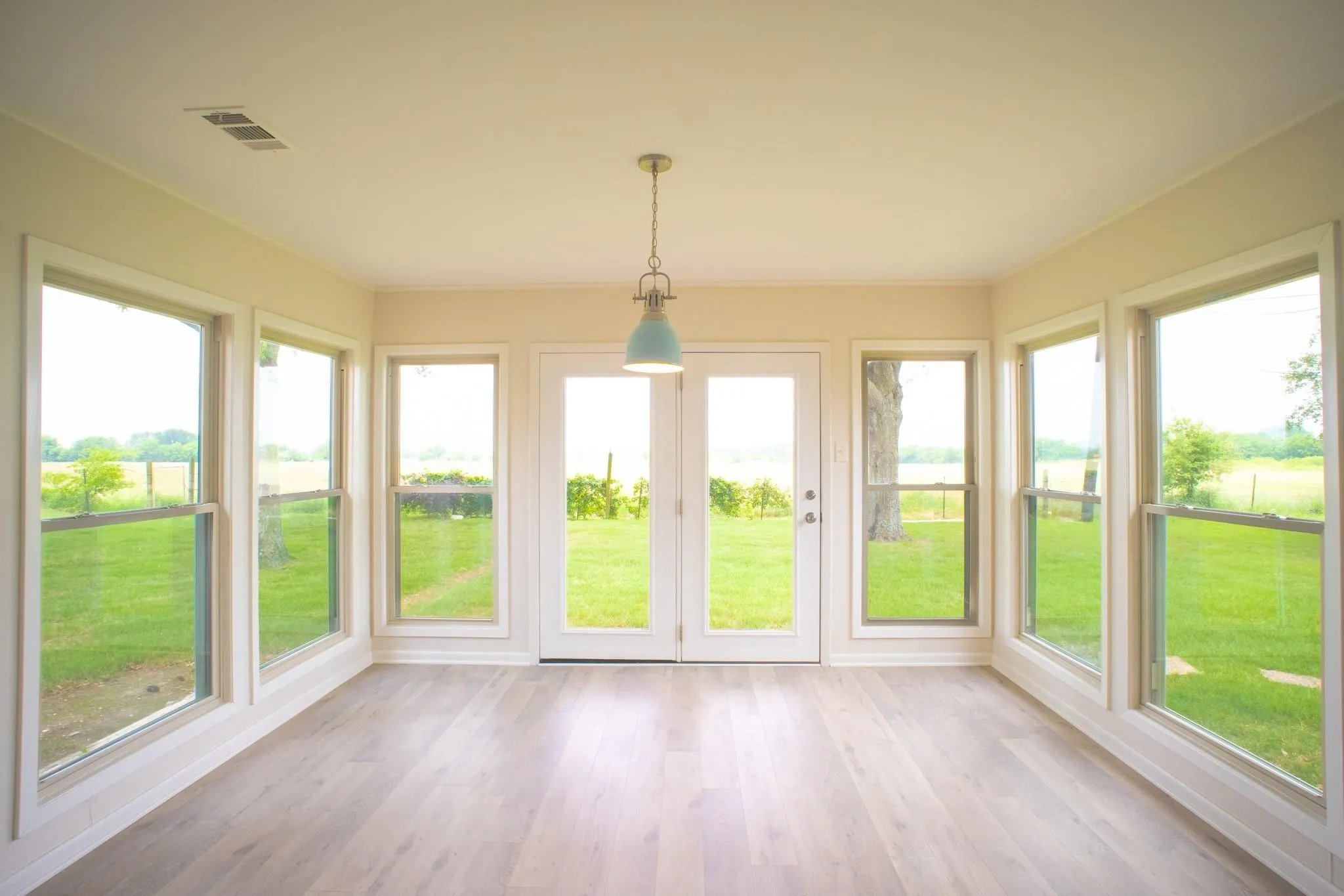 Sunroom featuring wood-finish flooring, white trim throughout, and a light blue pendant fixture