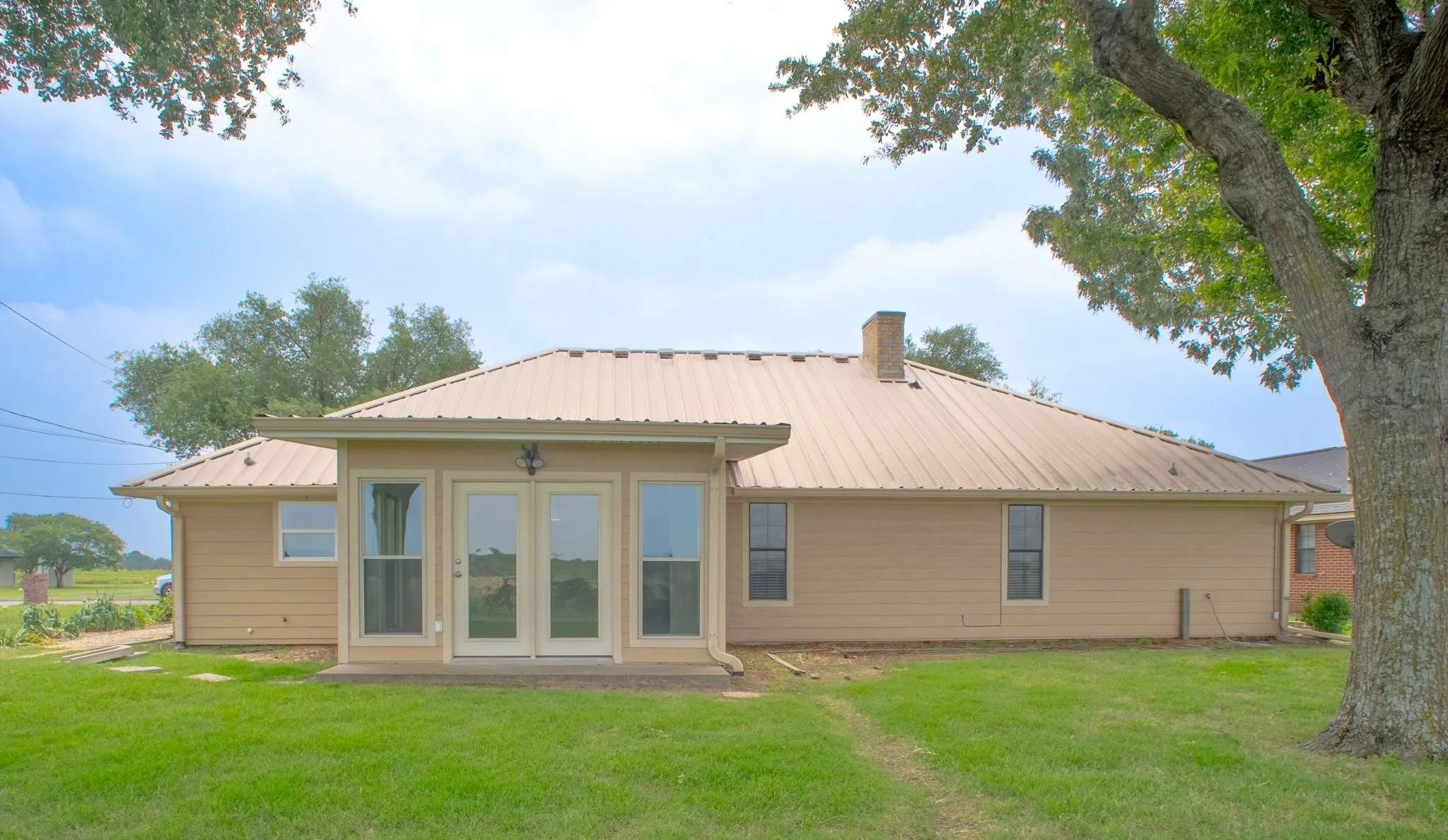 Expansive rear exterior featuring a tan metal roof, light beige siding, and a prominent brick chimney