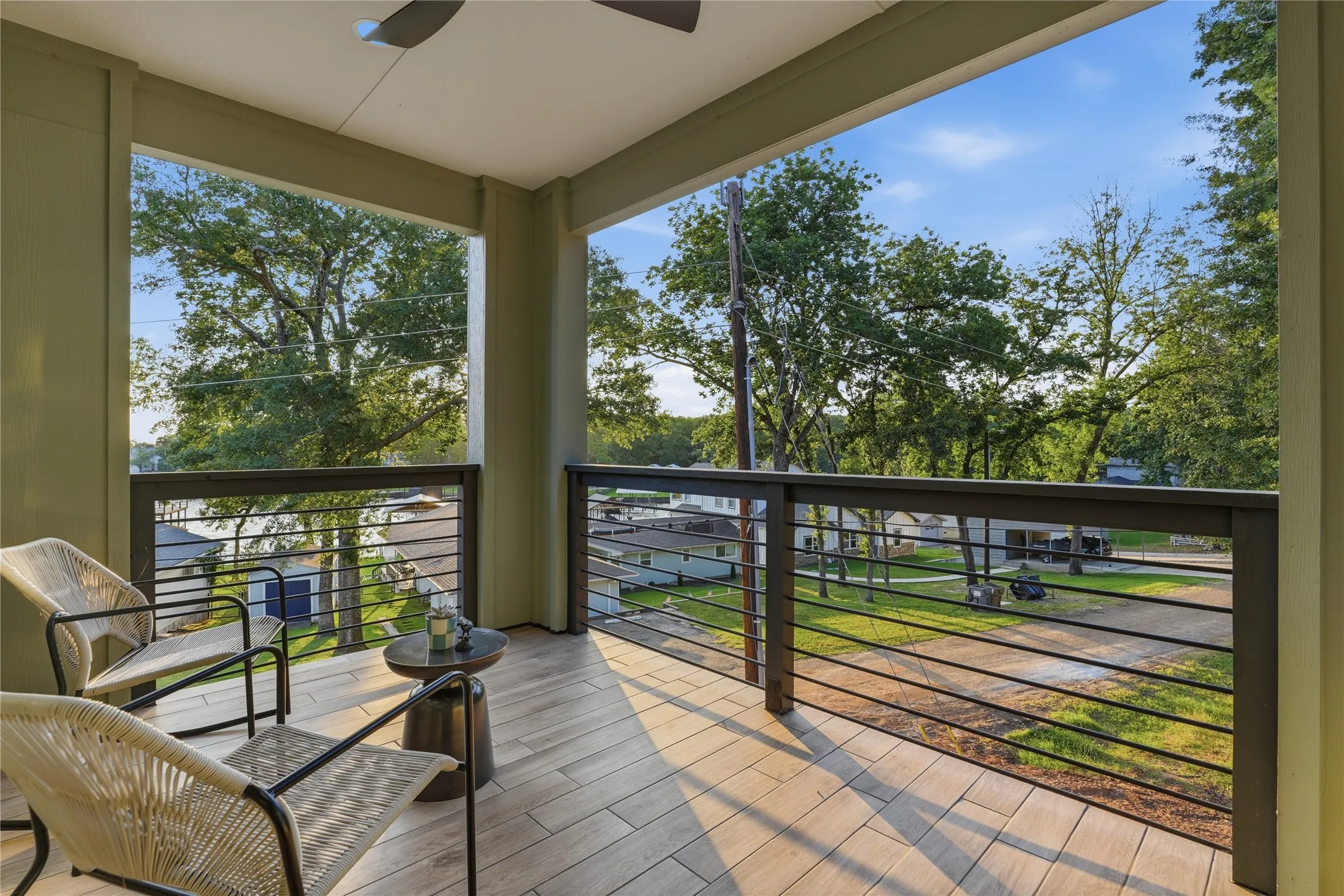 Covered balcony with wood-finish flooring, featuring a modern ceiling fan and cable railings