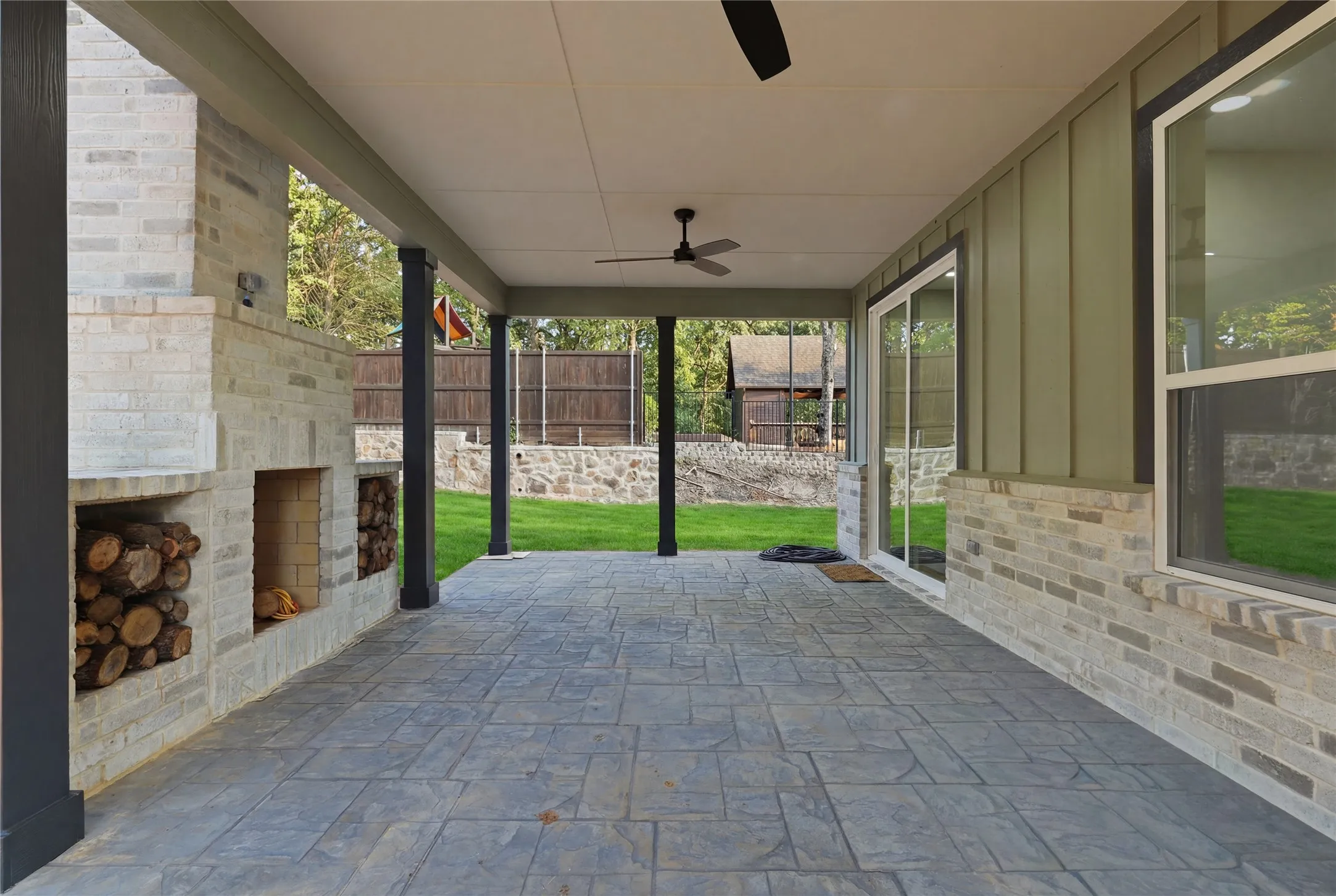 Covered patio featuring stamped concrete flooring and a white brick fireplace with integrated wood storage