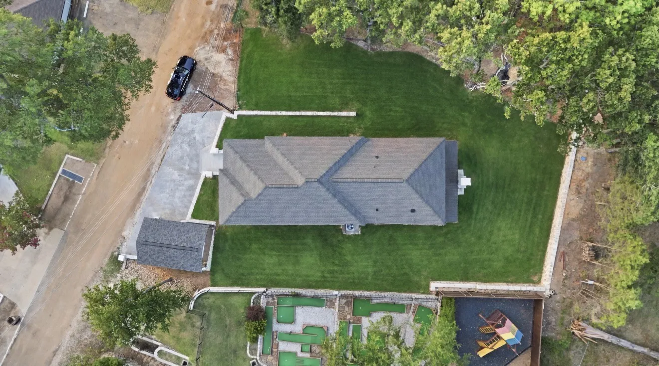Spacious property featuring a large main residence with a multi-gabled roof, extensive green lawn, and a separate detached structure