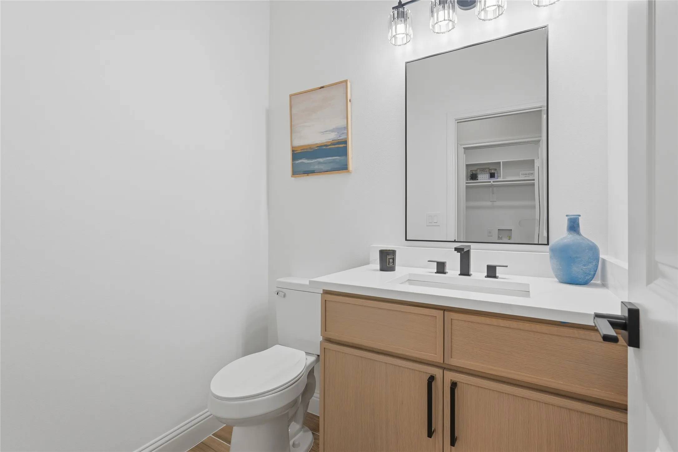 Powder room featuring a wood-finish vanity with black hardware, white countertop, integrated rectangular sink, and matte black faucet