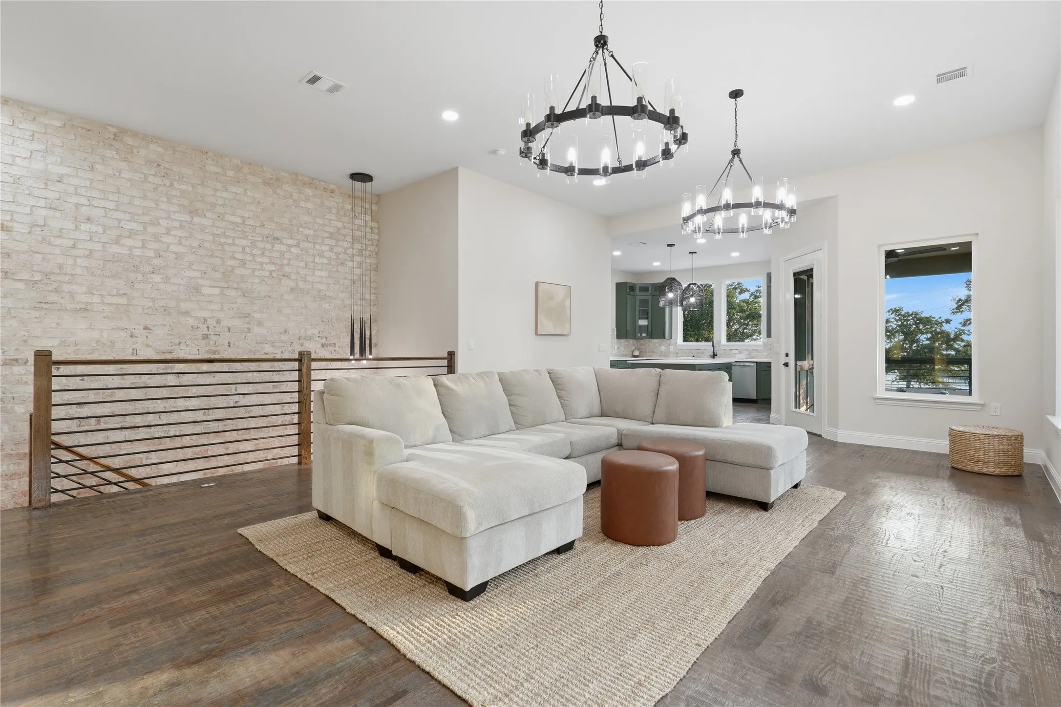 Spacious open-concept room featuring wood-finish flooring, a whitewashed brick accent wall, and contemporary chandeliers