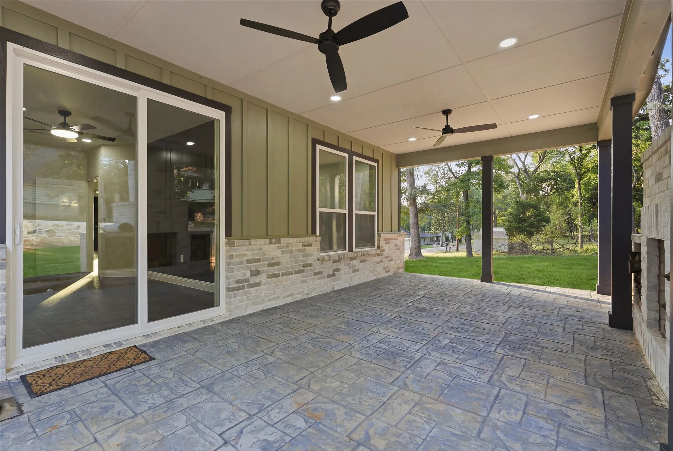 Expansive covered patio featuring stamped concrete flooring, multiple ceiling fans with integrated lighting, recessed lighting, and a stone-clad outdoor fireplace