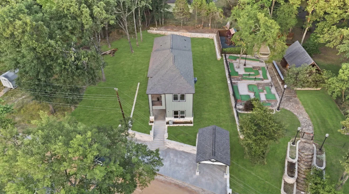 Aerial view of the property featuring a two-story residence, a detached carport, an integrated putting green, a stone pathway, and a tiered stone staircase