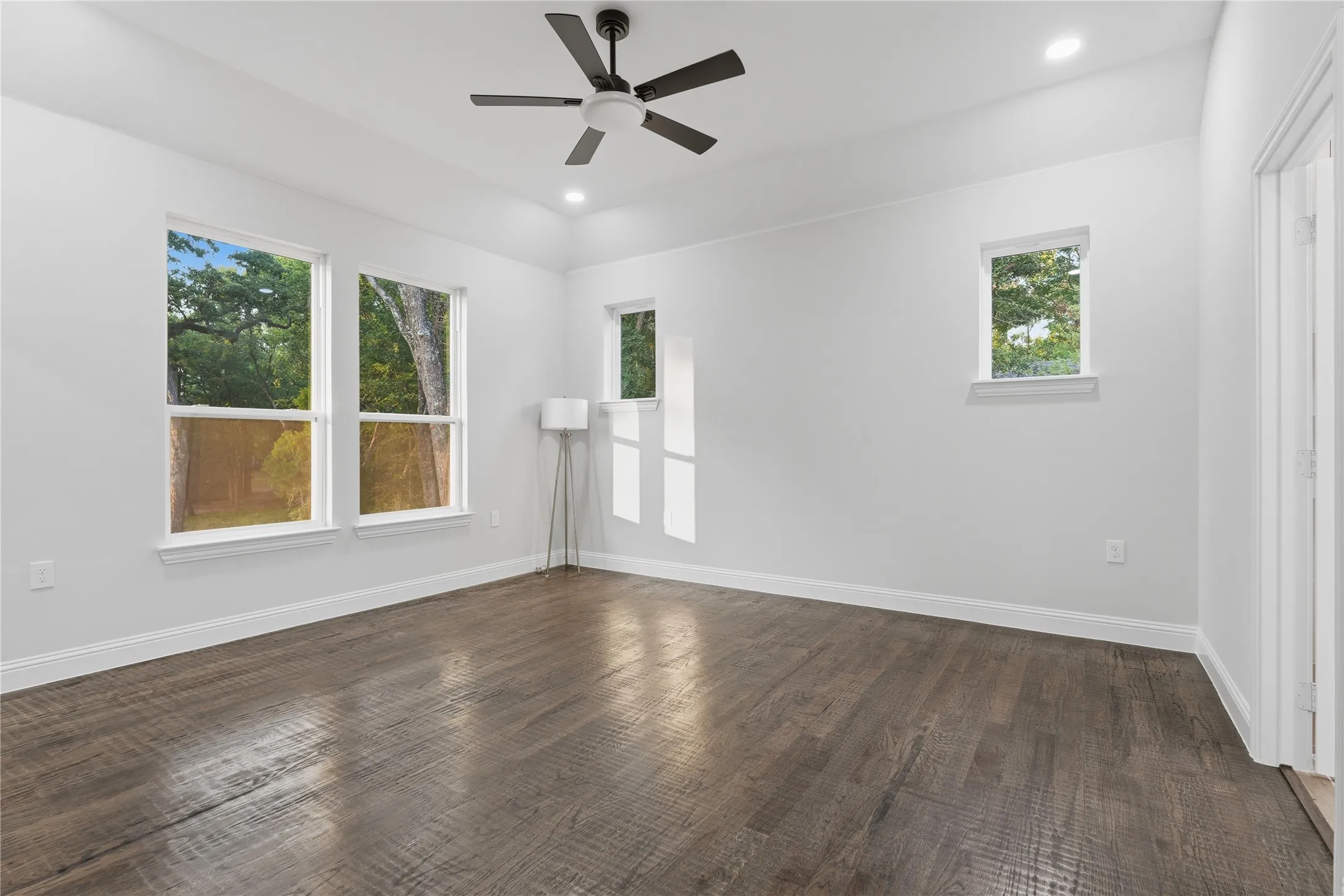 Spacious room featuring wood-finish flooring, white walls, and multiple windows