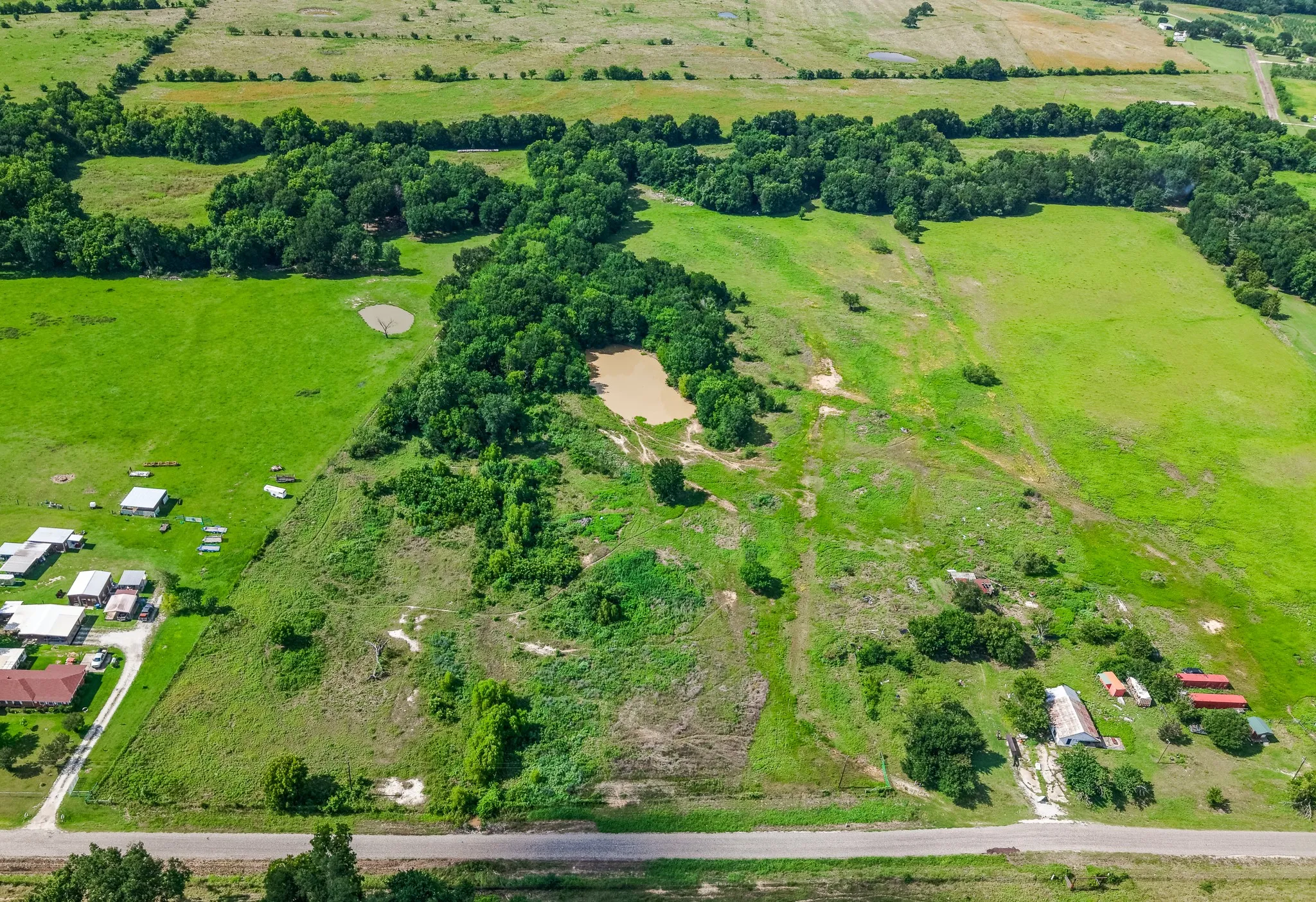 Expansive land parcel featuring open green fields, wooded areas, multiple ponds, and existing structures