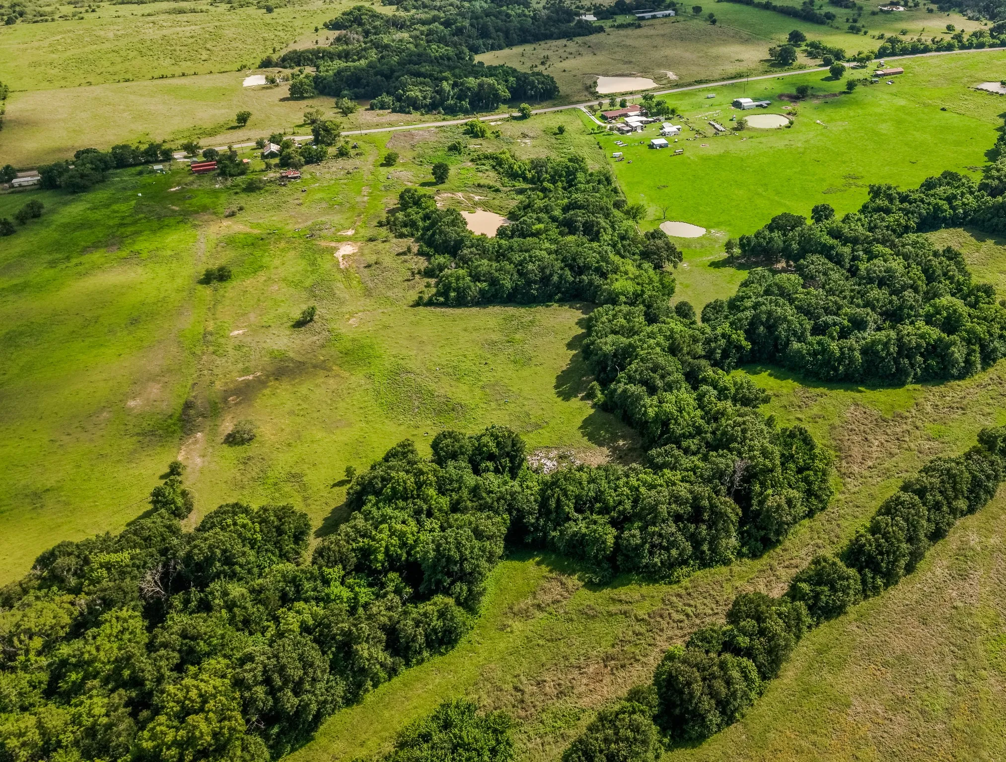 Expansive green acreage featuring scattered tree lines, multiple water features, and distant rural structures
