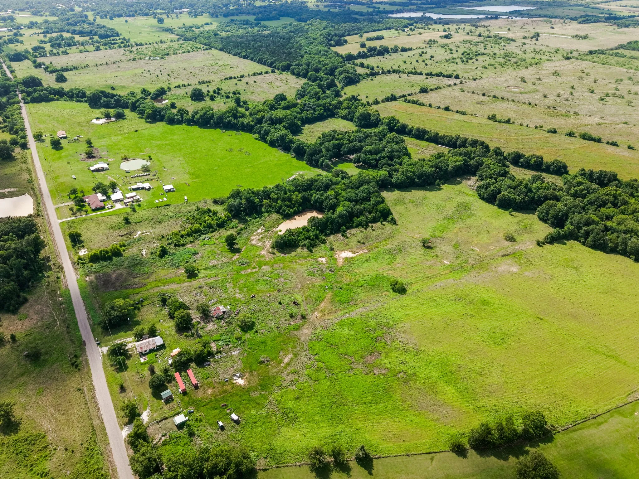 Expansive green pastures with scattered tree lines and multiple residential structures