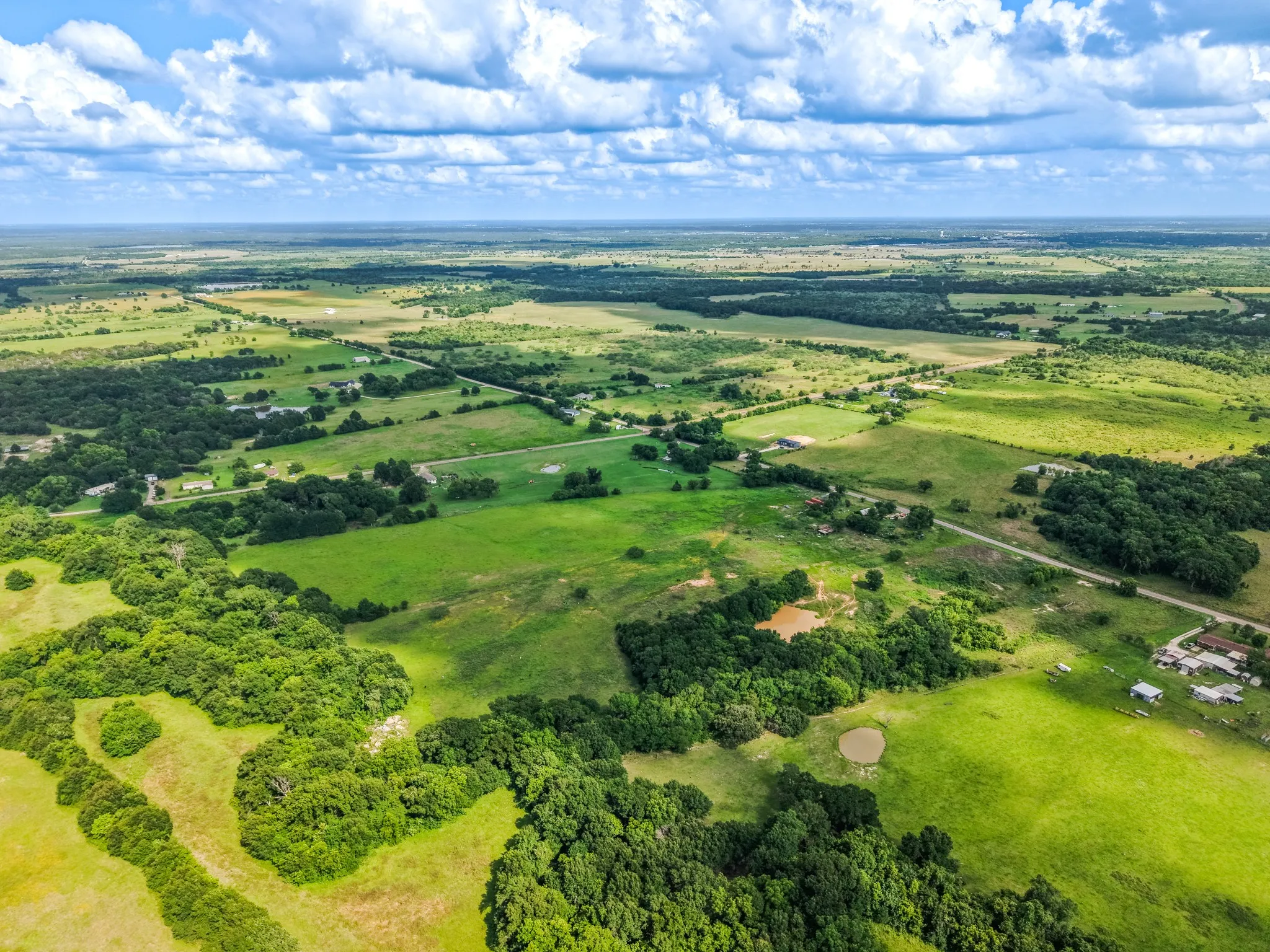 Expansive aerial perspective showcasing a vast landscape of green fields and scattered treelines