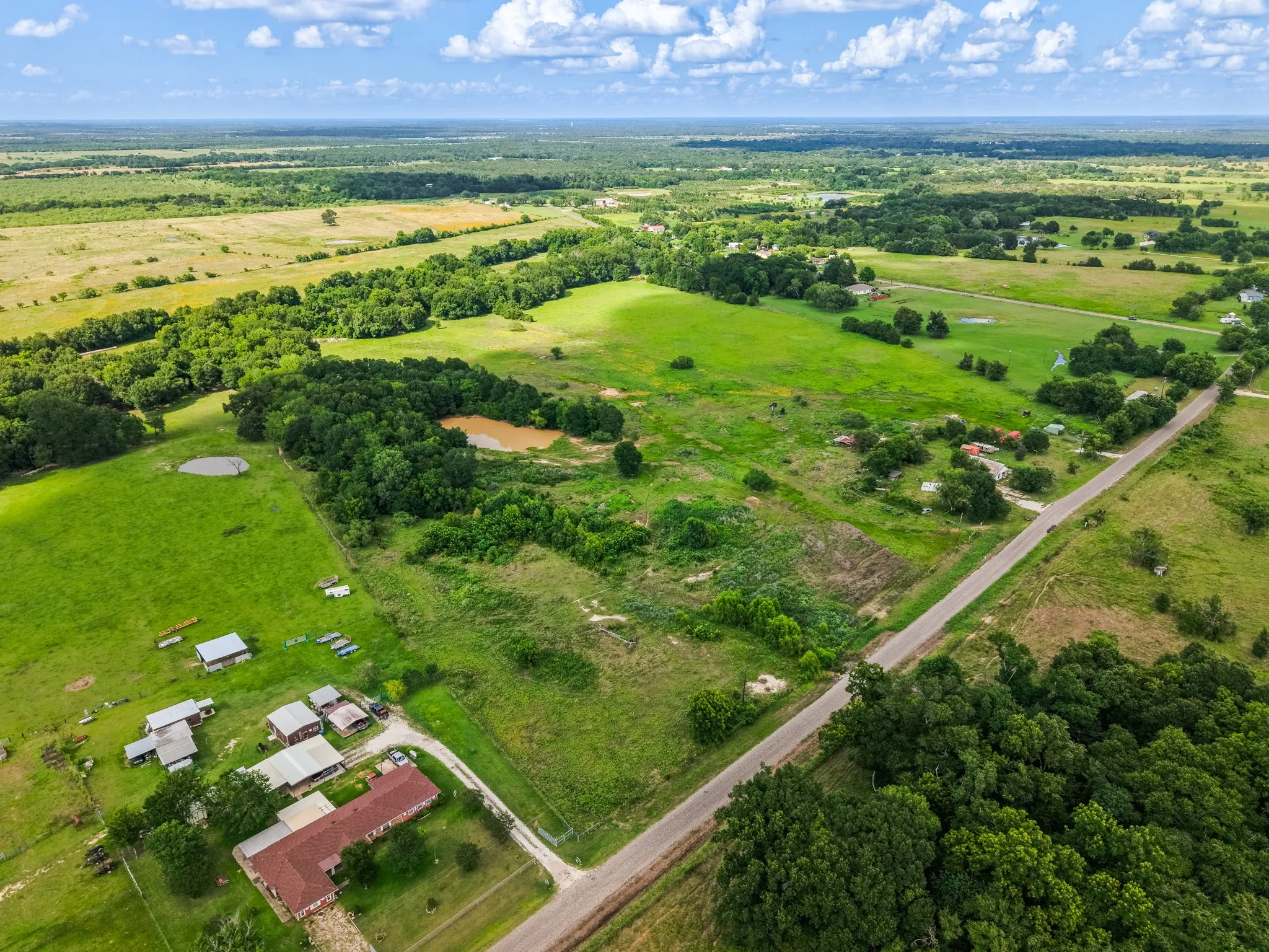 Expansive rural landscape featuring a paved road, multiple buildings, and two ponds
