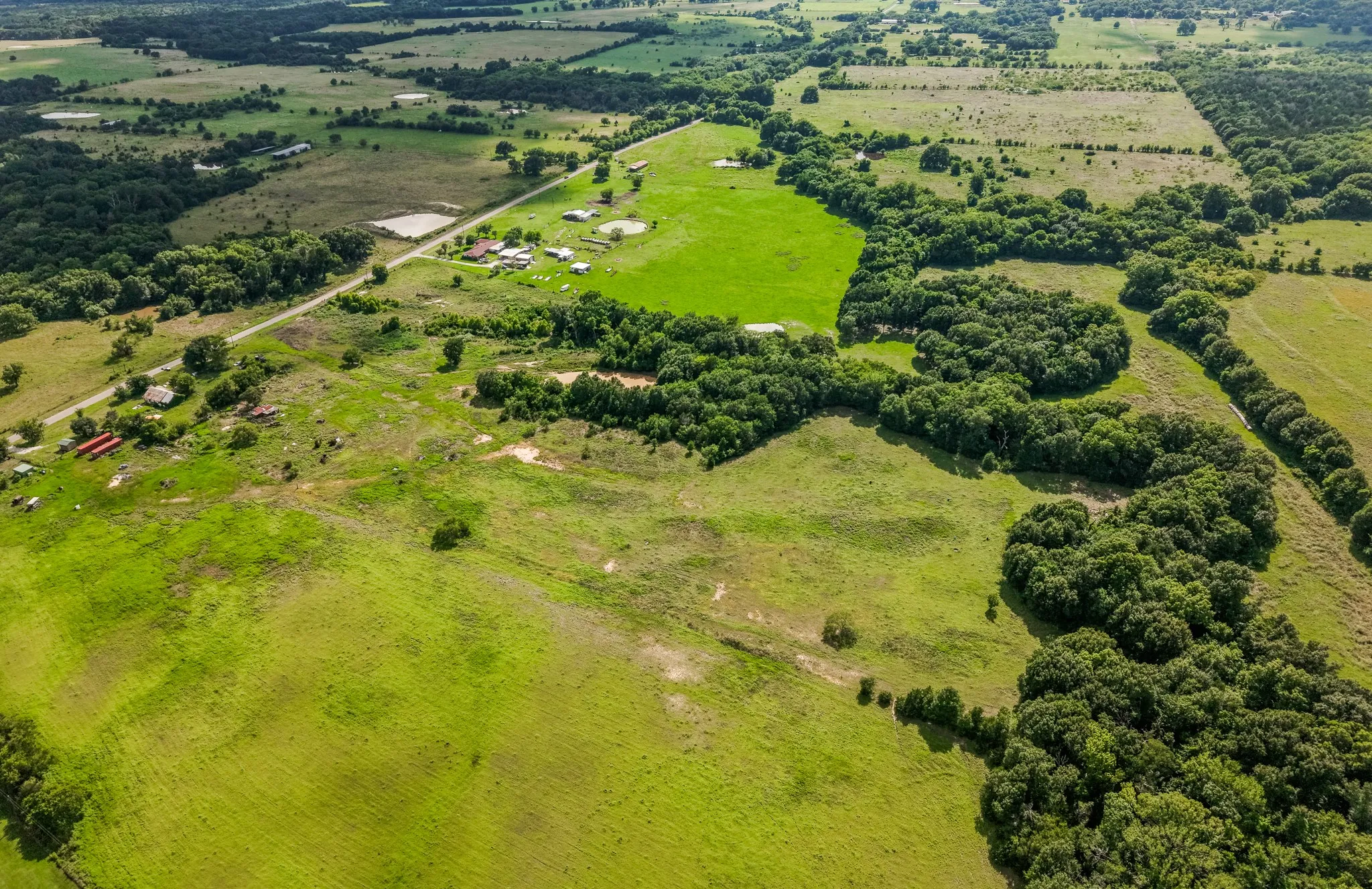 Expansive acreage featuring abundant green pastures, mature tree lines, and multiple structures