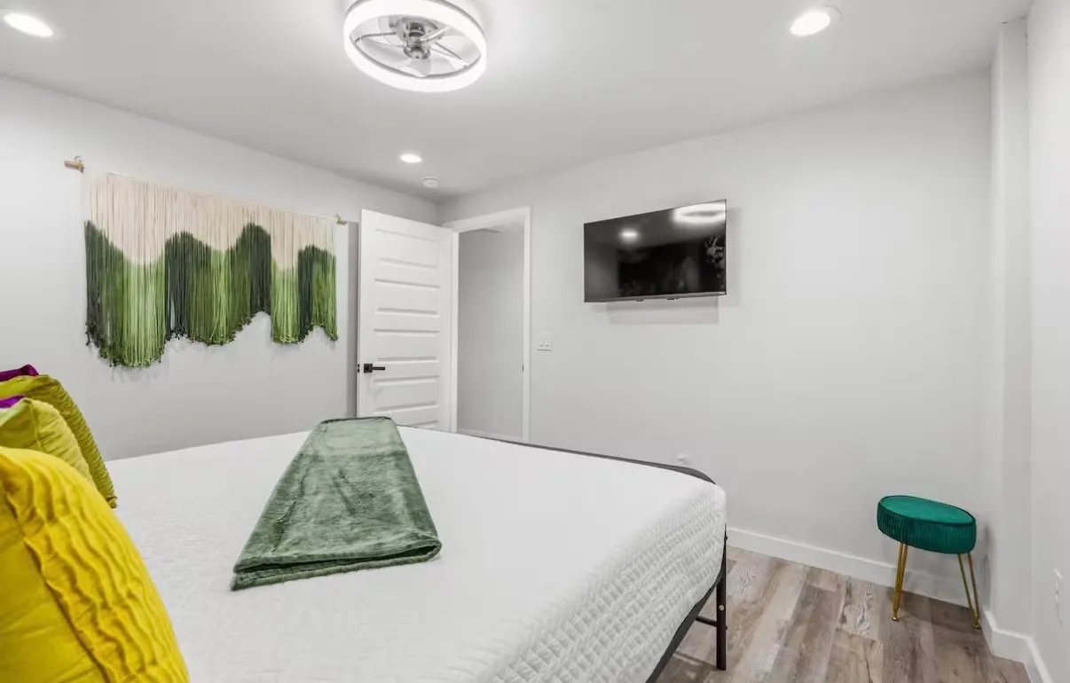 Bedroom featuring light wood-finish flooring, a contemporary ceiling fan, recessed lighting, a mounted flat-screen display, and a paneled door with black hardware