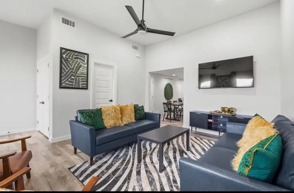 Spacious living area featuring light wood-finish flooring, a contemporary black ceiling fan, and a neutral color palette