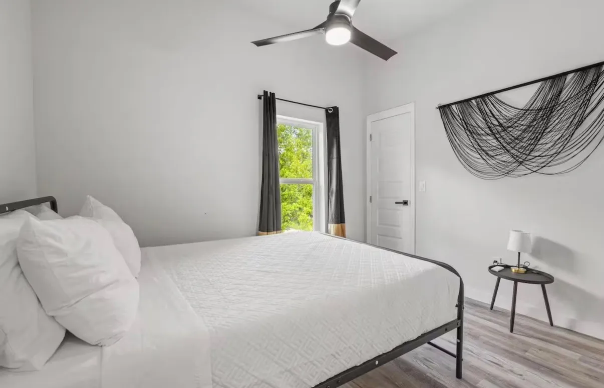 Spacious room featuring wood-finish flooring, a contemporary ceiling fan, and a window with dark curtains