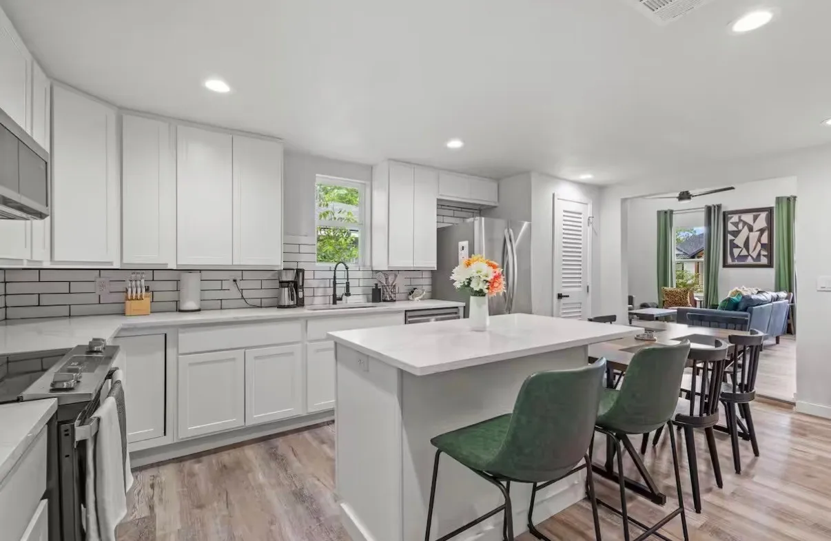 Modern kitchen featuring a central island with countertop seating, white shaker cabinetry, stainless steel appliances, light wood-finish flooring, and subway tile backsplash