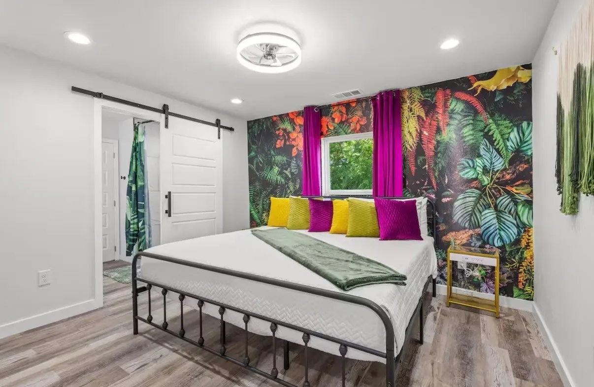 Bedroom featuring a barn door leading to an en-suite, wood-finish flooring, recessed lighting, a window with magenta drapes, and a vibrant accent wall
