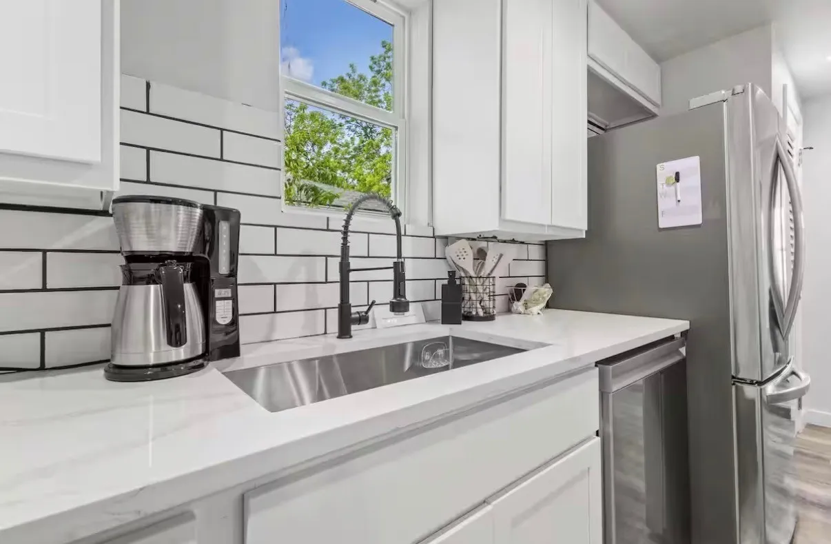 Sleek kitchen featuring white cabinetry, a large single-basin stainless steel sink with a matte black gooseneck faucet, a subway tile backsplash, and a stainless steel dishwasher
