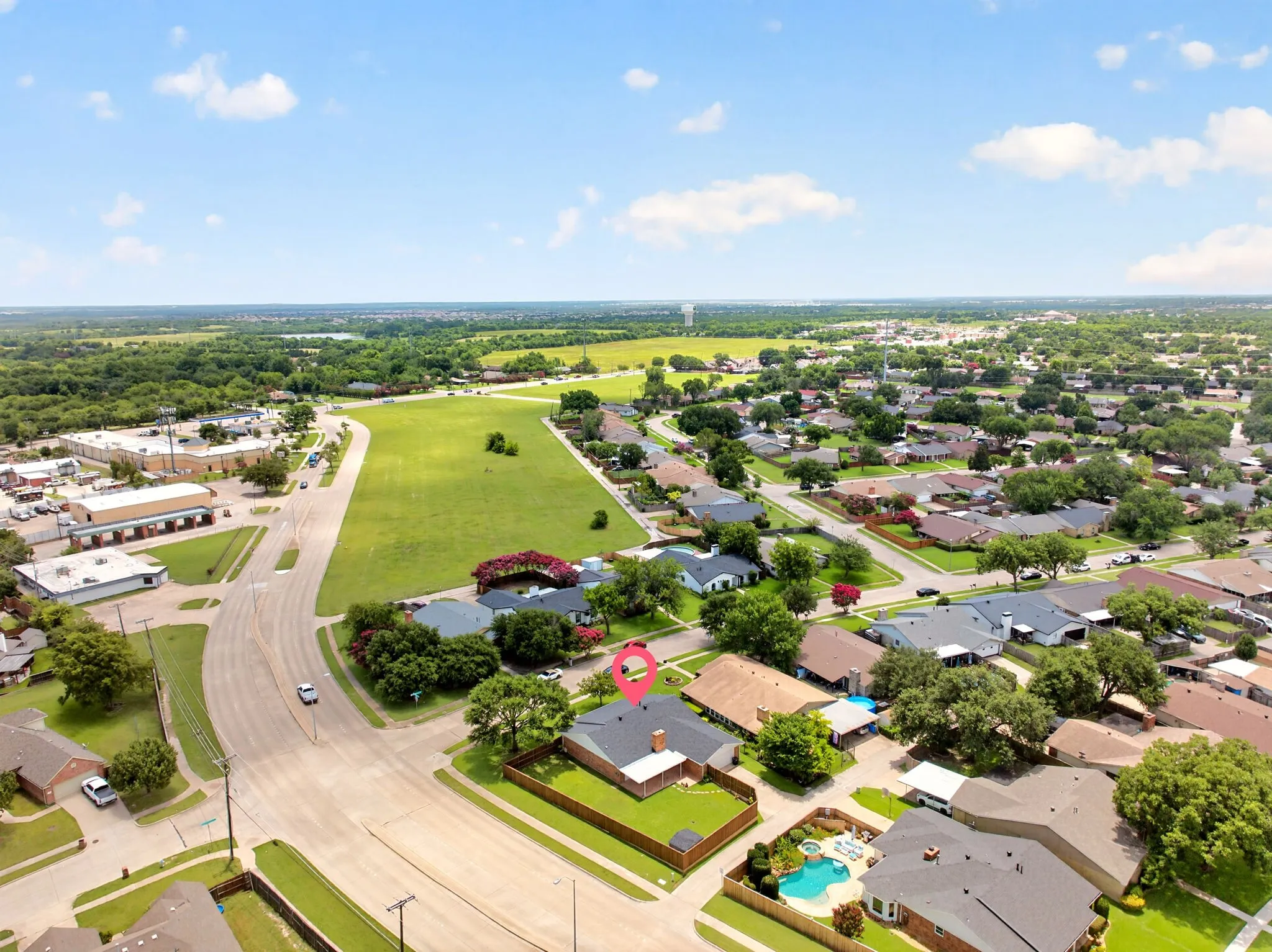 Aerial perspective showcasing a residential property with a dark shingle roof and a fenced backyard, surrounded by established neighborhood trees