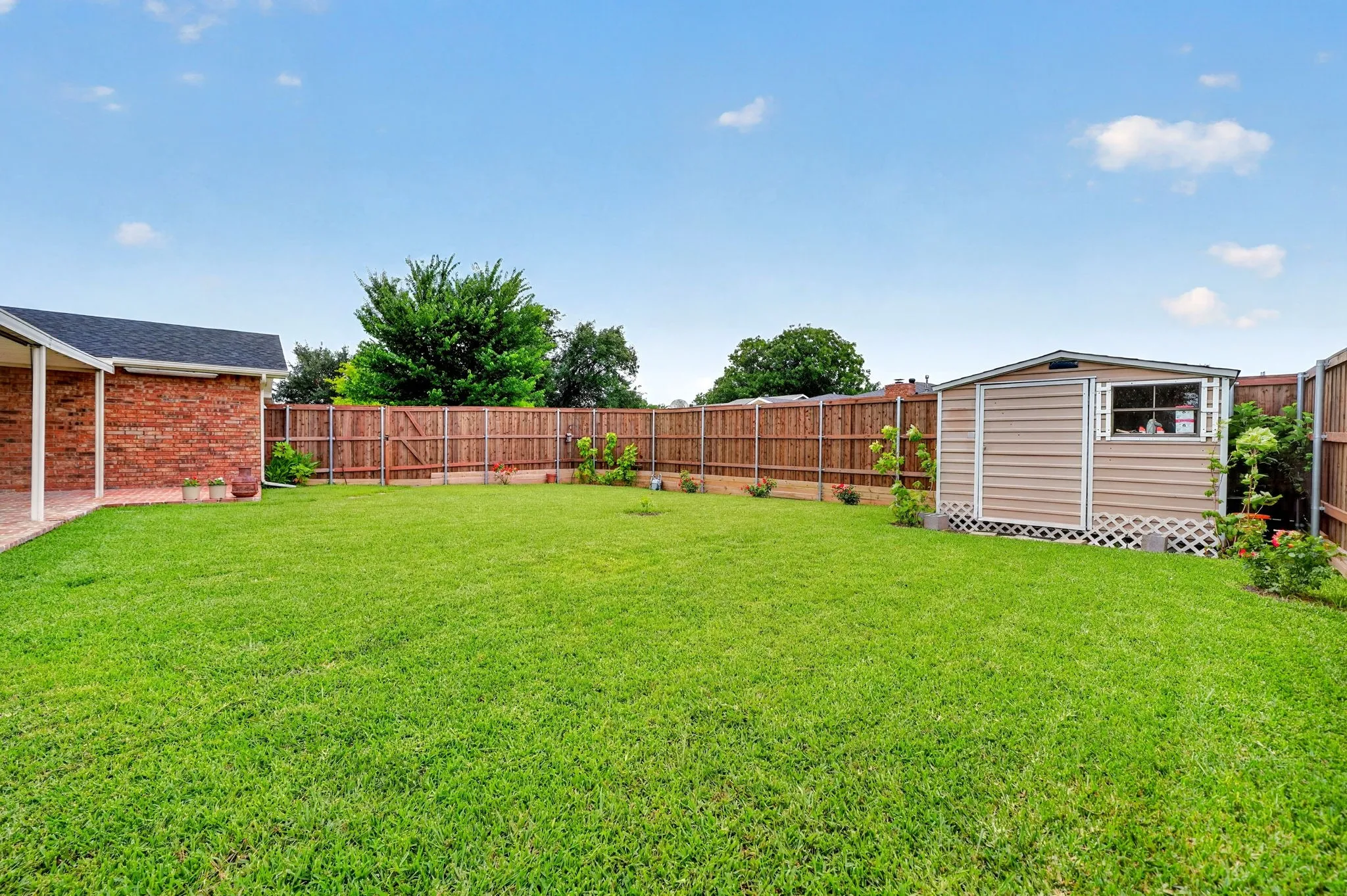 Expansive backyard featuring a large green lawn, full privacy fencing, and a dedicated storage shed