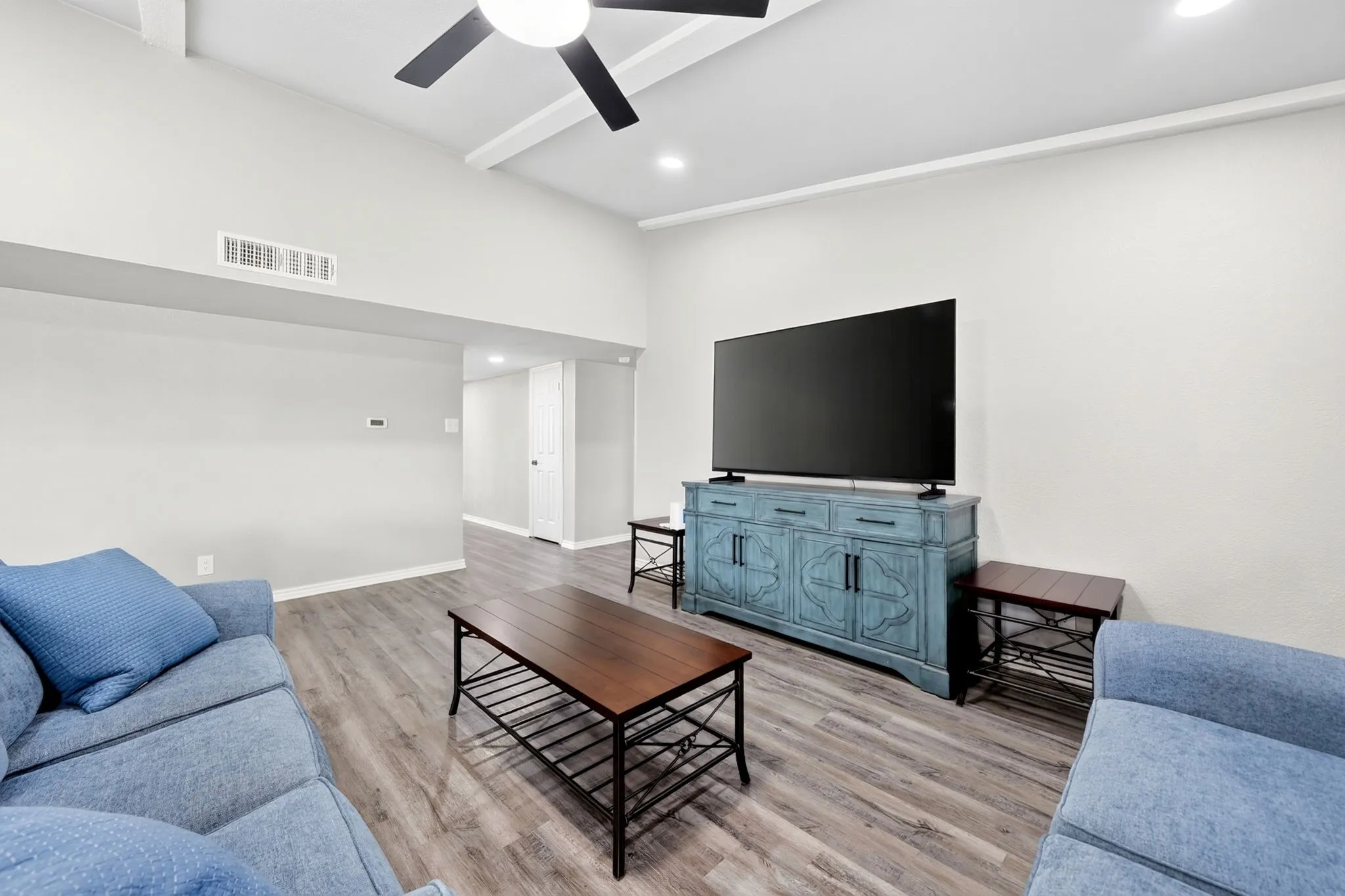 Living area featuring vaulted ceilings with exposed beams, wood-finish flooring, recessed lighting, and a ceiling fan