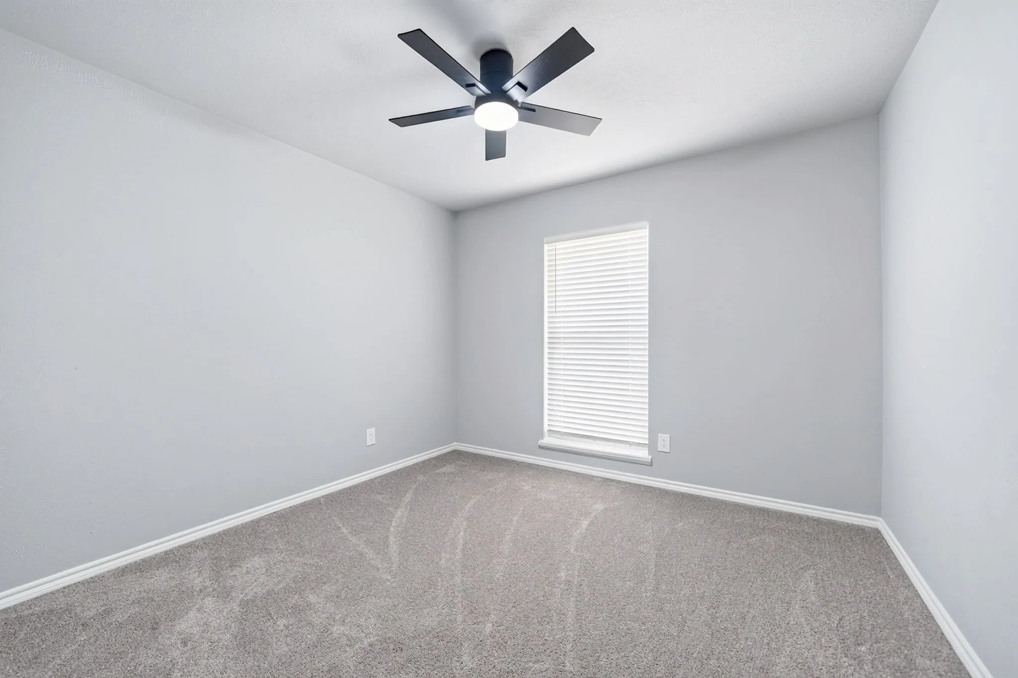 Room featuring light gray walls, gray carpeting, white baseboards, and a window with white blinds