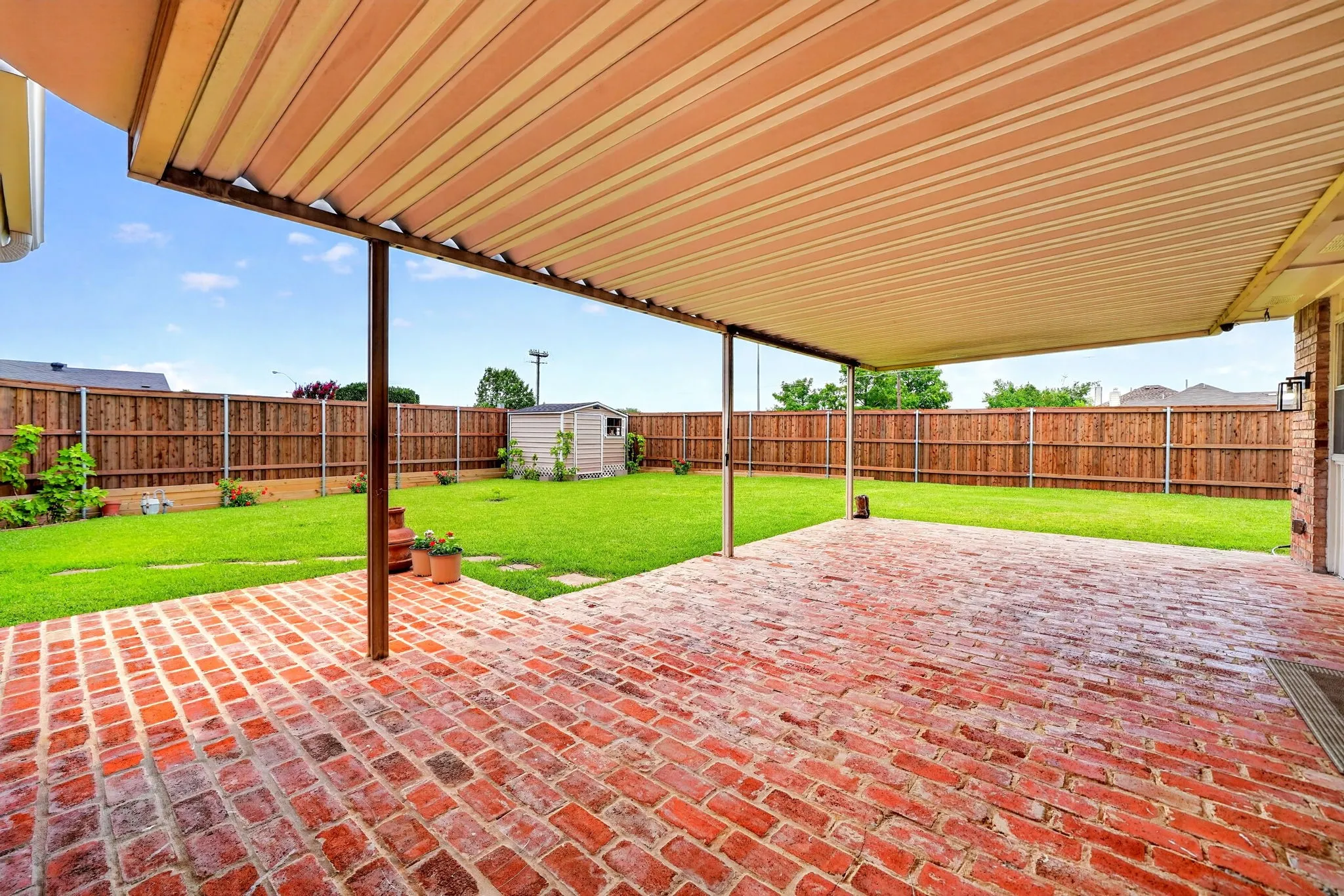 Expansive covered patio featuring red brick paving and a metal awning