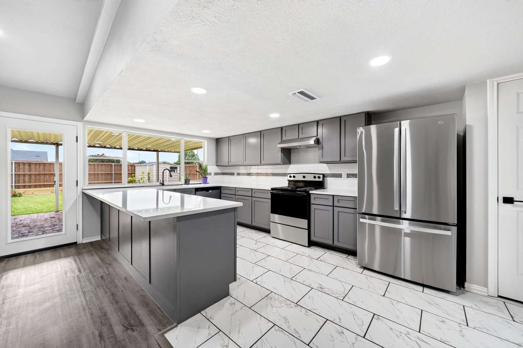 Modern kitchen featuring a large central island with a light-toned countertop, gray cabinetry, stainless steel appliances, and recessed lighting