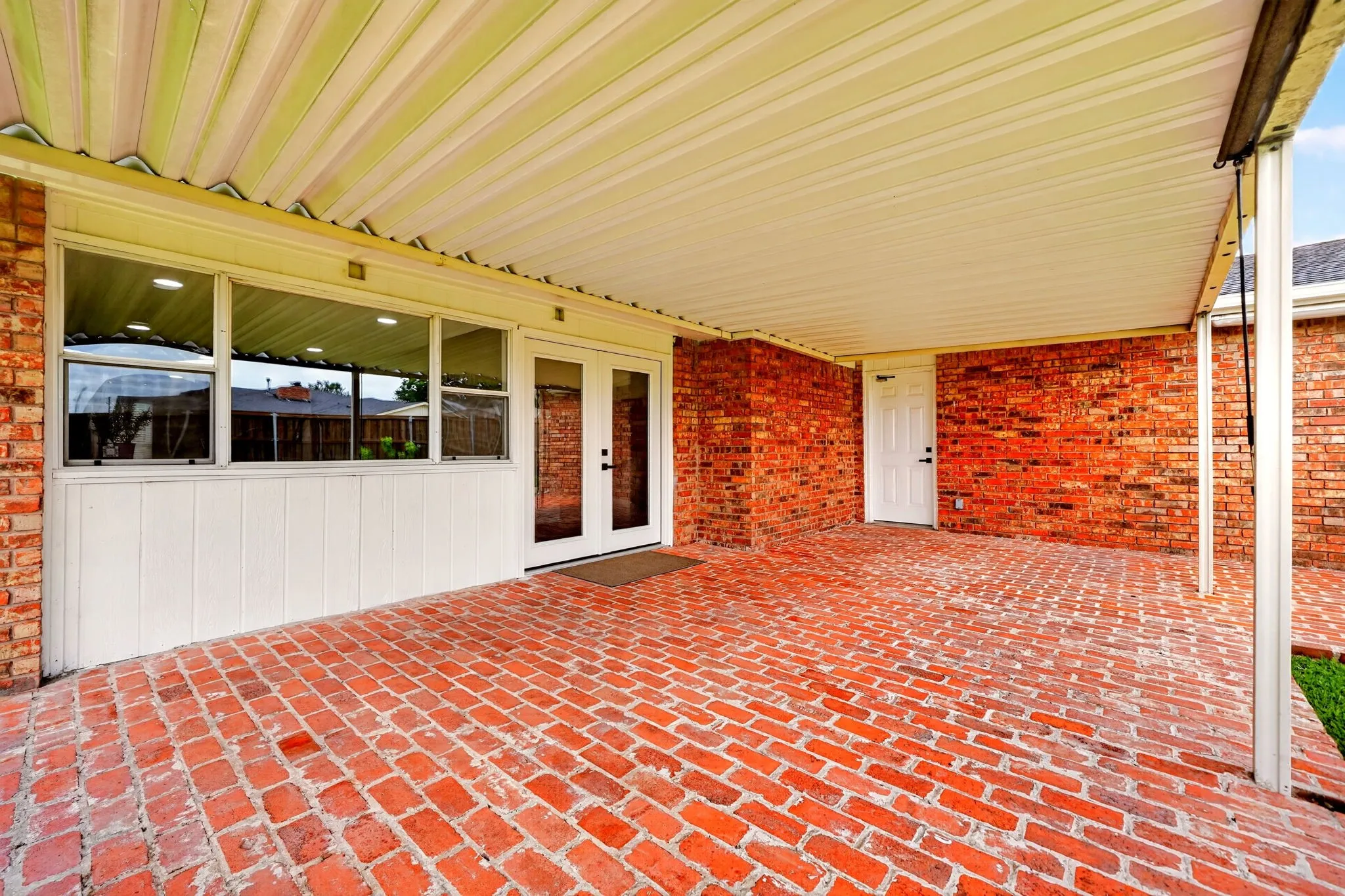 Expansive covered patio featuring brick paver flooring and a white corrugated roof