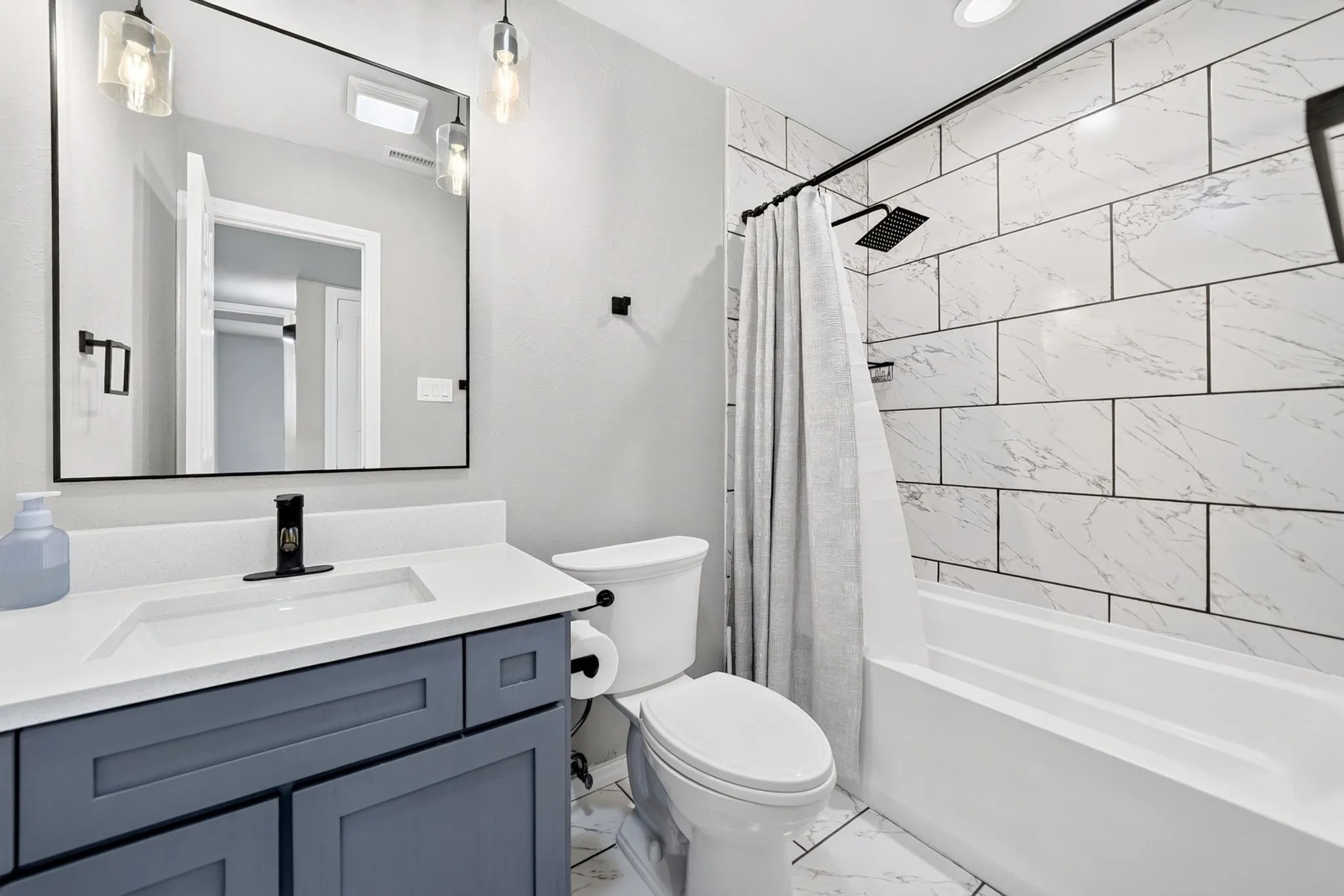 Bathroom featuring a white subway tile shower surround with black fixtures, a white bathtub, and a dark blue vanity with a white countertop and rectangular sink