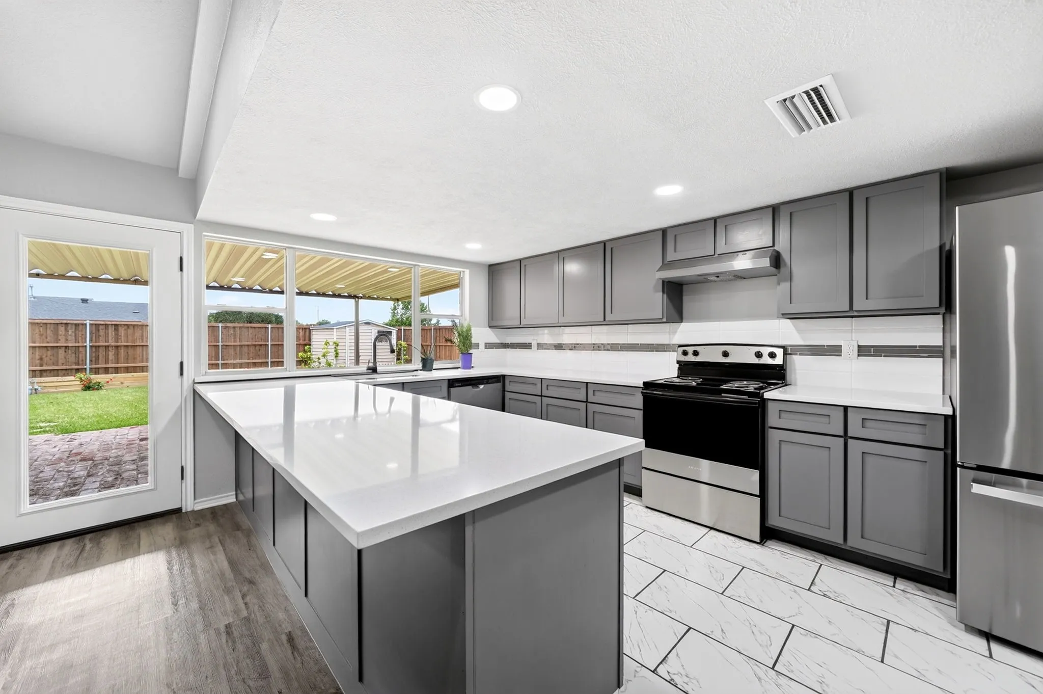Kitchen featuring a spacious island with a white countertop, grey cabinetry, stainless steel appliances, and wood-finish flooring