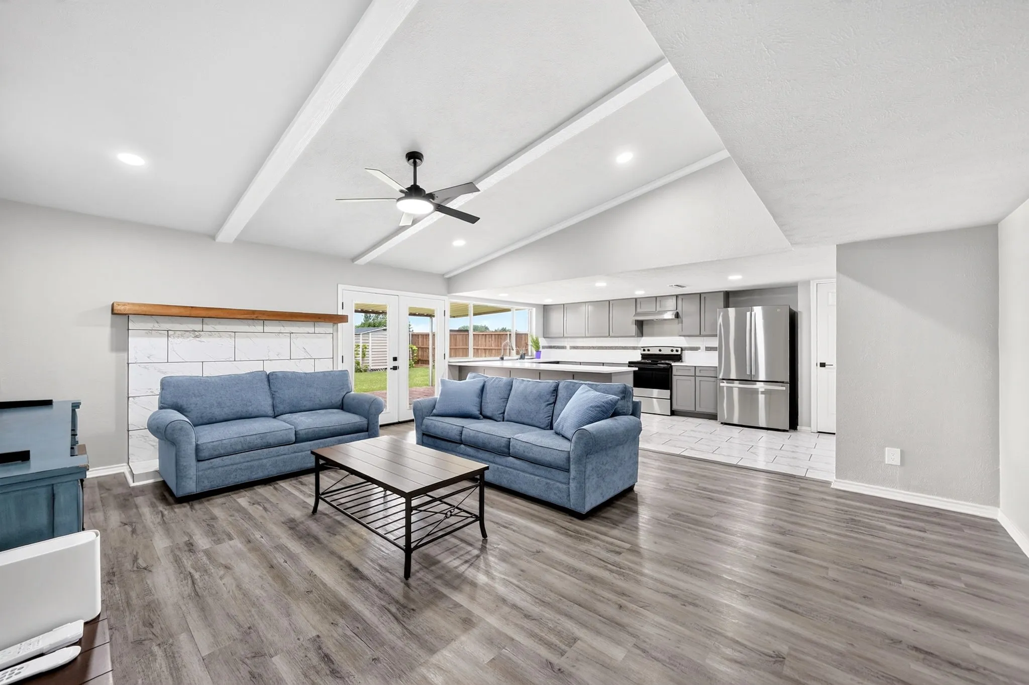 Open-concept living space with vaulted ceilings, exposed beams, and contemporary ceiling fan