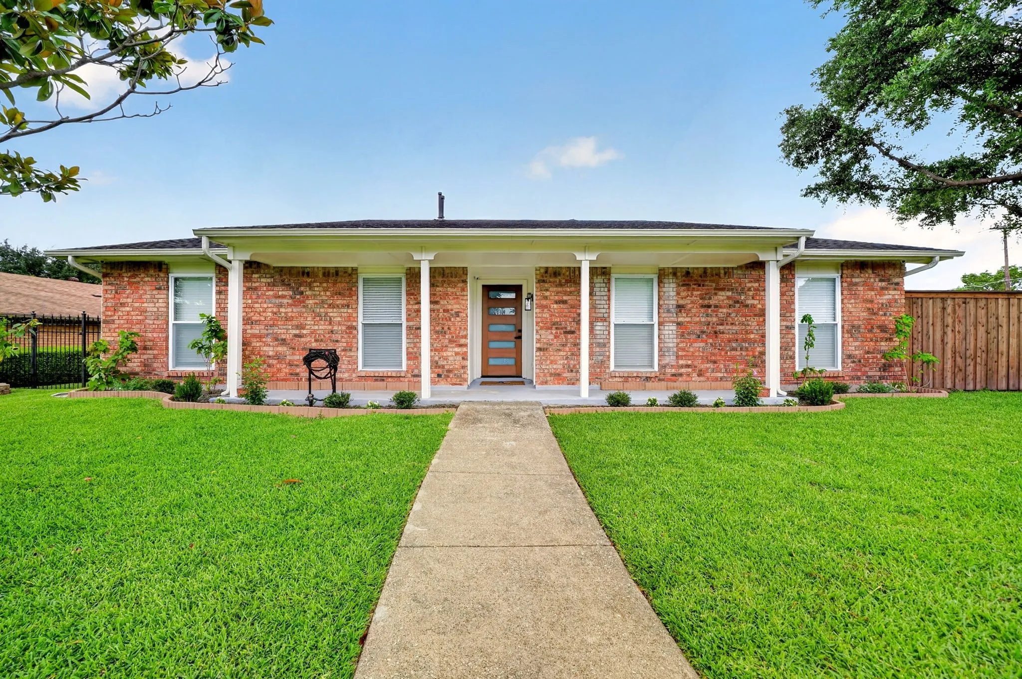 Traditional brick exterior with white trim, a covered front porch supported by white columns, a modern front door, and a concrete walkway