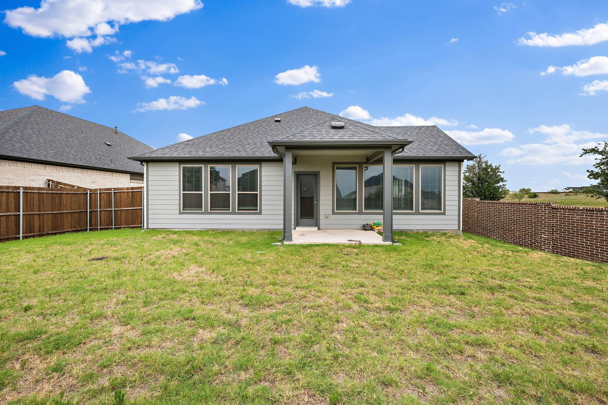 Expansive backyard featuring a covered patio, multiple windows, a wood fence, and a brick privacy wall