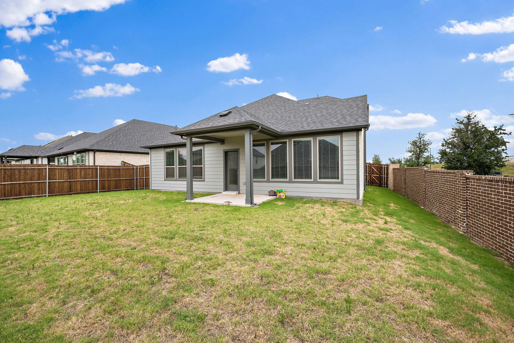 Expansive backyard featuring a covered patio, brick perimeter fencing, and a wood privacy fence
