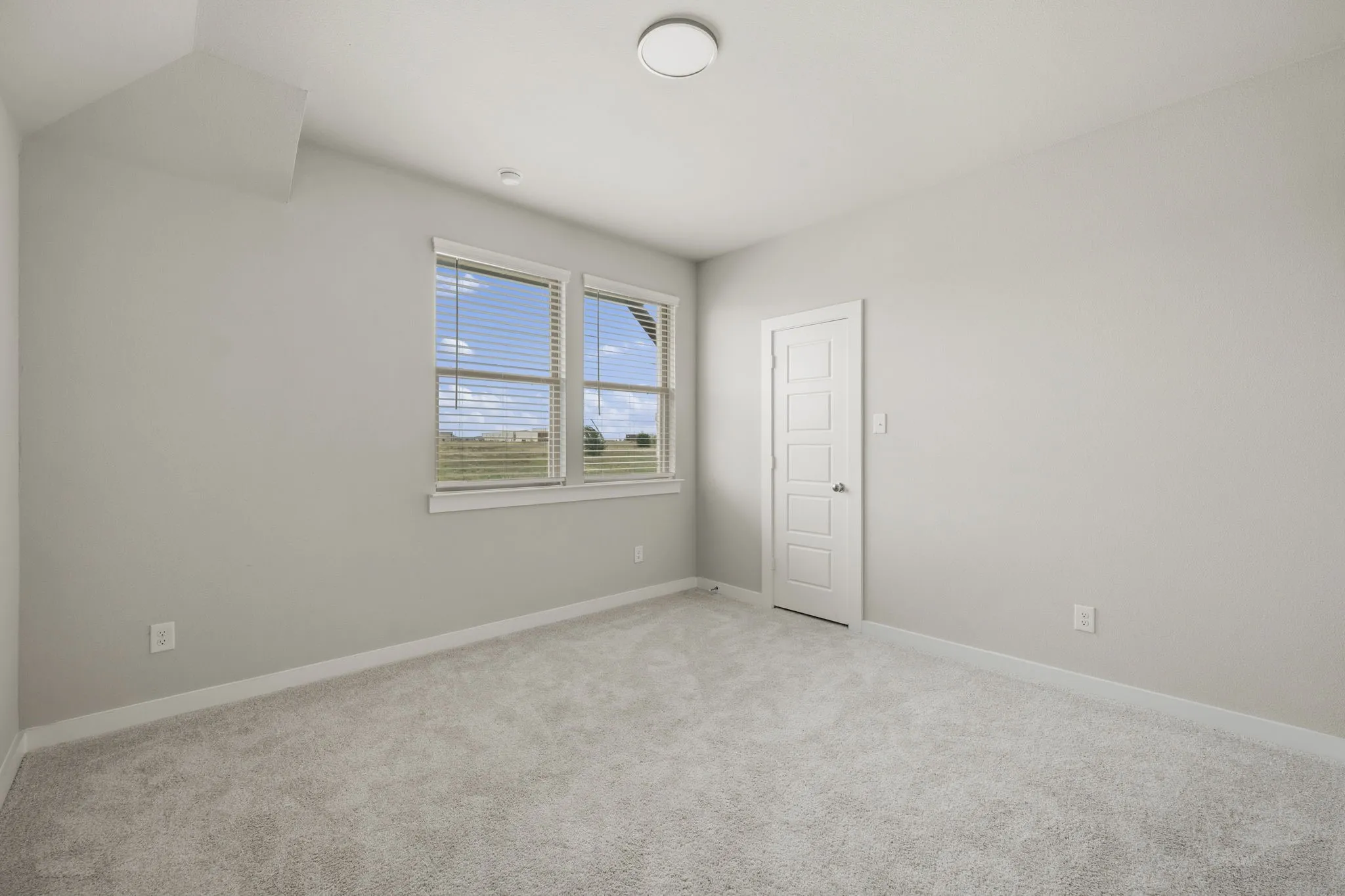 Bright room featuring two windows with horizontal blinds, light gray wall paint, and gray carpet flooring