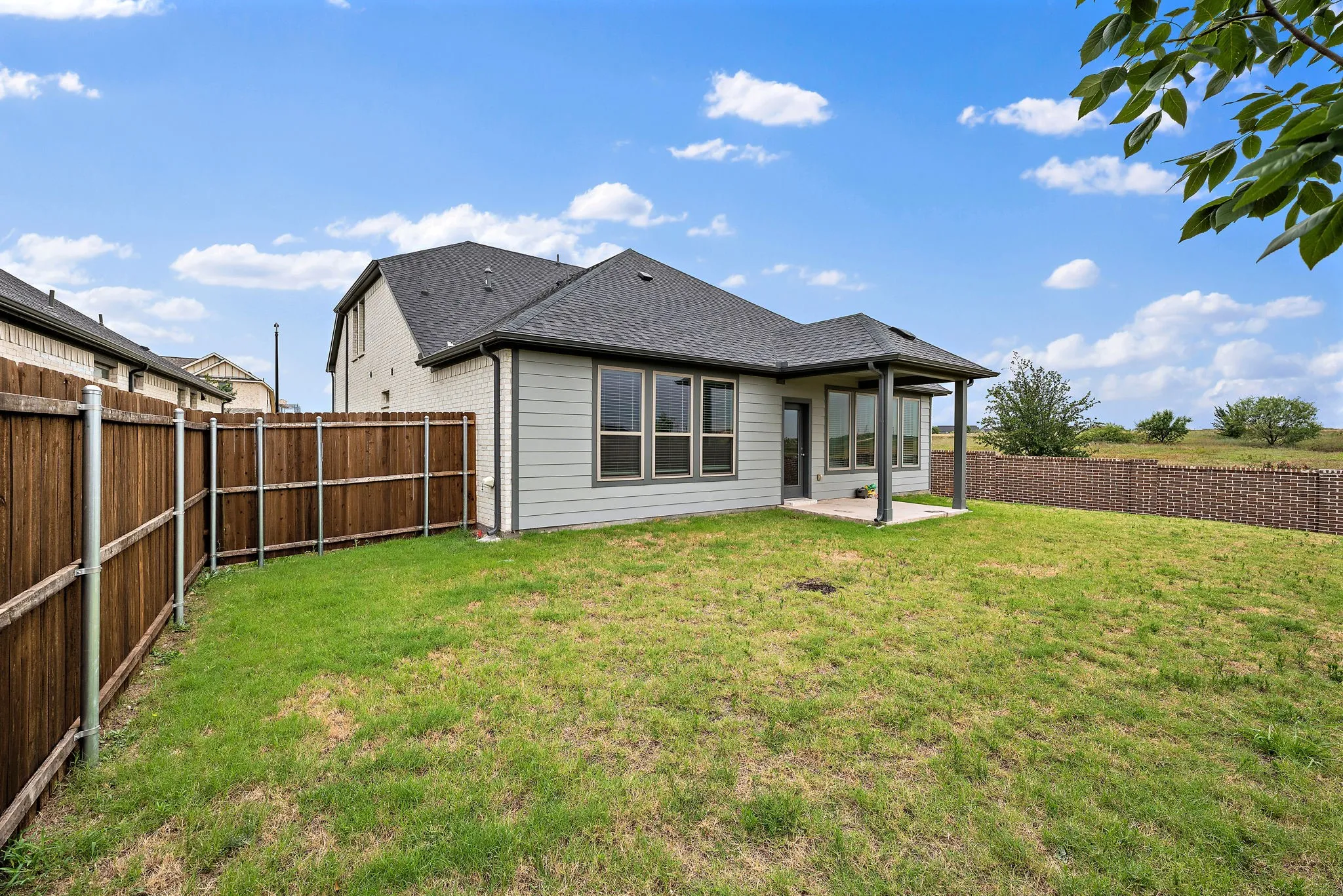 Expansive rear yard featuring a covered patio with concrete flooring, multiple large windows, and a combination of wood and decorative fencing