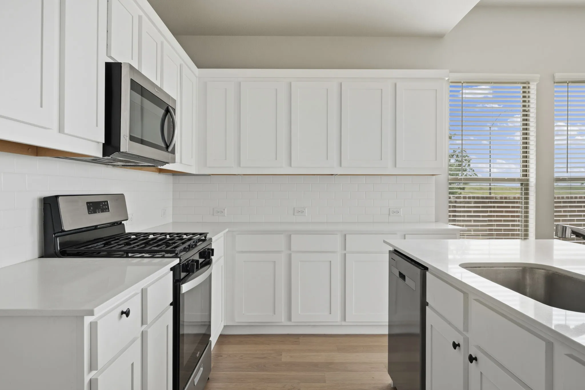 Modern kitchen featuring white cabinetry, light-toned countertops, a stainless steel microwave, a black and stainless steel range, and wood-finish flooring