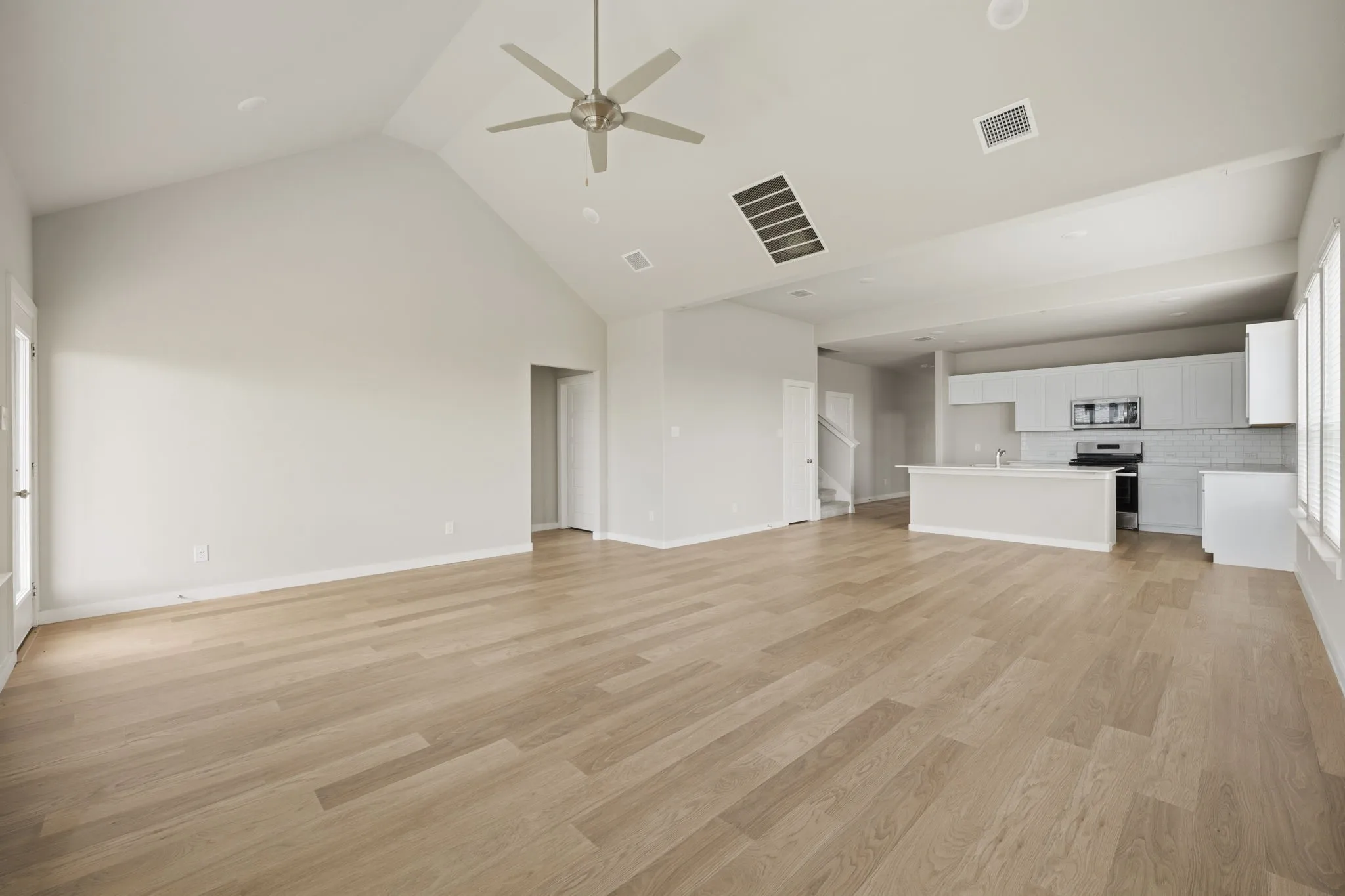 Open-concept living space featuring wood-finish flooring, a vaulted ceiling with a ceiling fan, and recessed lighting