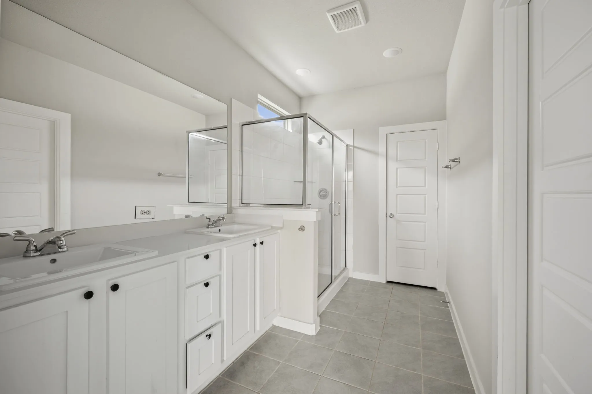 Bathroom featuring a double vanity with white cabinetry and dark hardware, dual undermount sinks, and a seamless glass shower enclosure with tiled walls