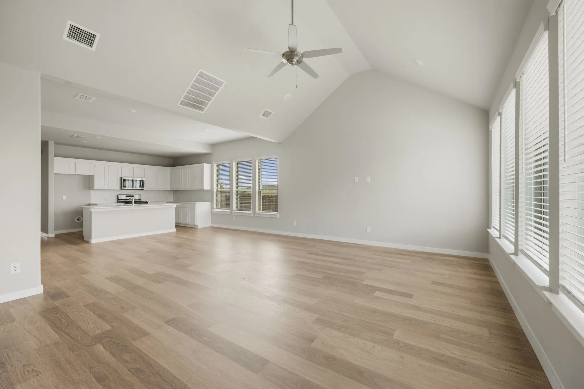 Open-concept living space featuring wood-finish flooring, a vaulted ceiling, and ample natural light from multiple windows